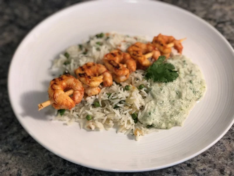 tandoori shrimp skewers on a plate with rice and cucumber raita