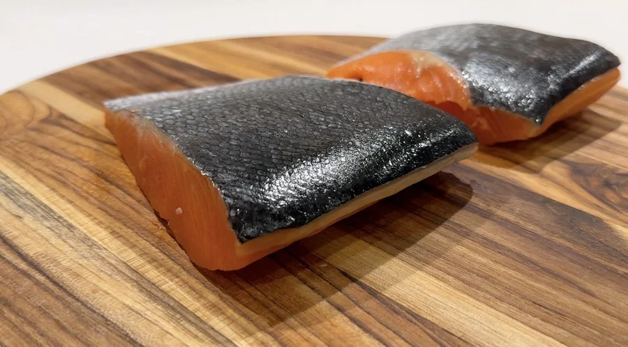 Two raw salmon fillets with skin on, perfect for making delicious air fryer salmon on a wooden cutting board.
