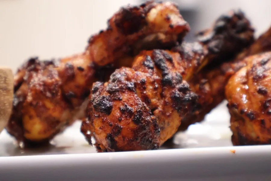 Close-up of air fryer tandoori chicken drumsticks, grilled and charred, stacked on a white plate.
