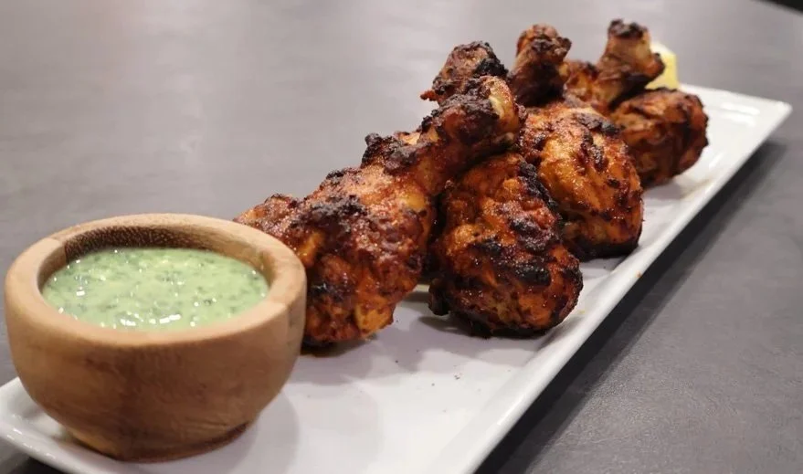 Air fryer tandoori chicken drumsticks on a rectangular white plate with a small bowl of green dipping sauce.