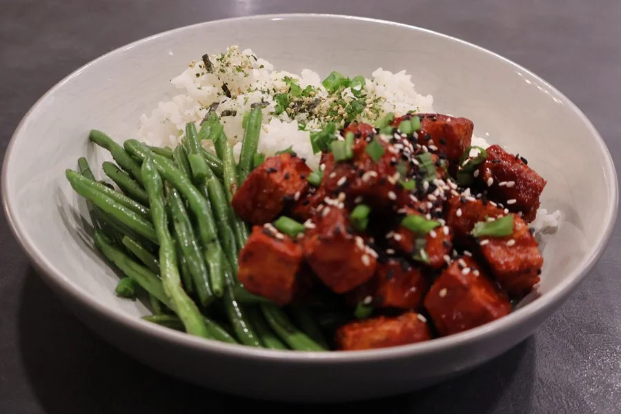 A bowl with white rice, green beans, and air fryer tofu cubes glazed and topped with sesame seeds, garnished with green onions.