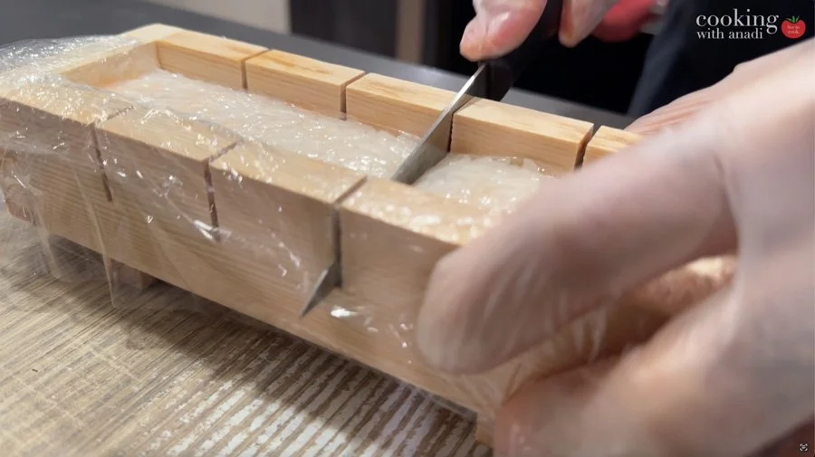 cutting pieces of sushi over plastic wrap