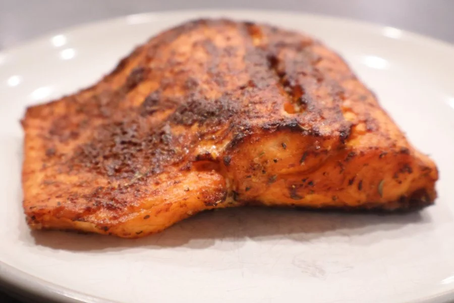 A piece of air fryer salmon seasoned with spices sits on a plain white plate.