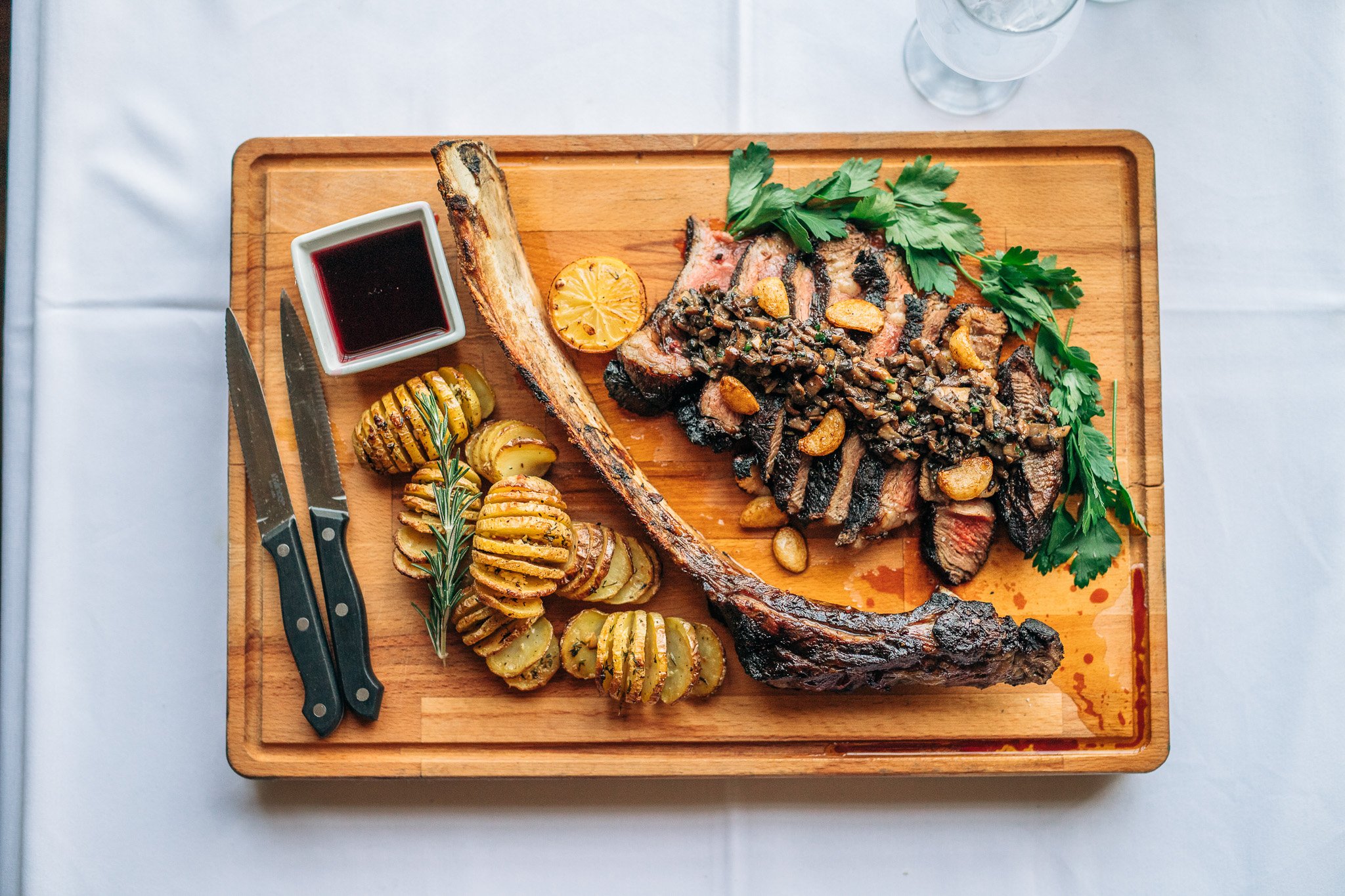 Tomahawk steak, roasted potatoes, and herbs on wooden board