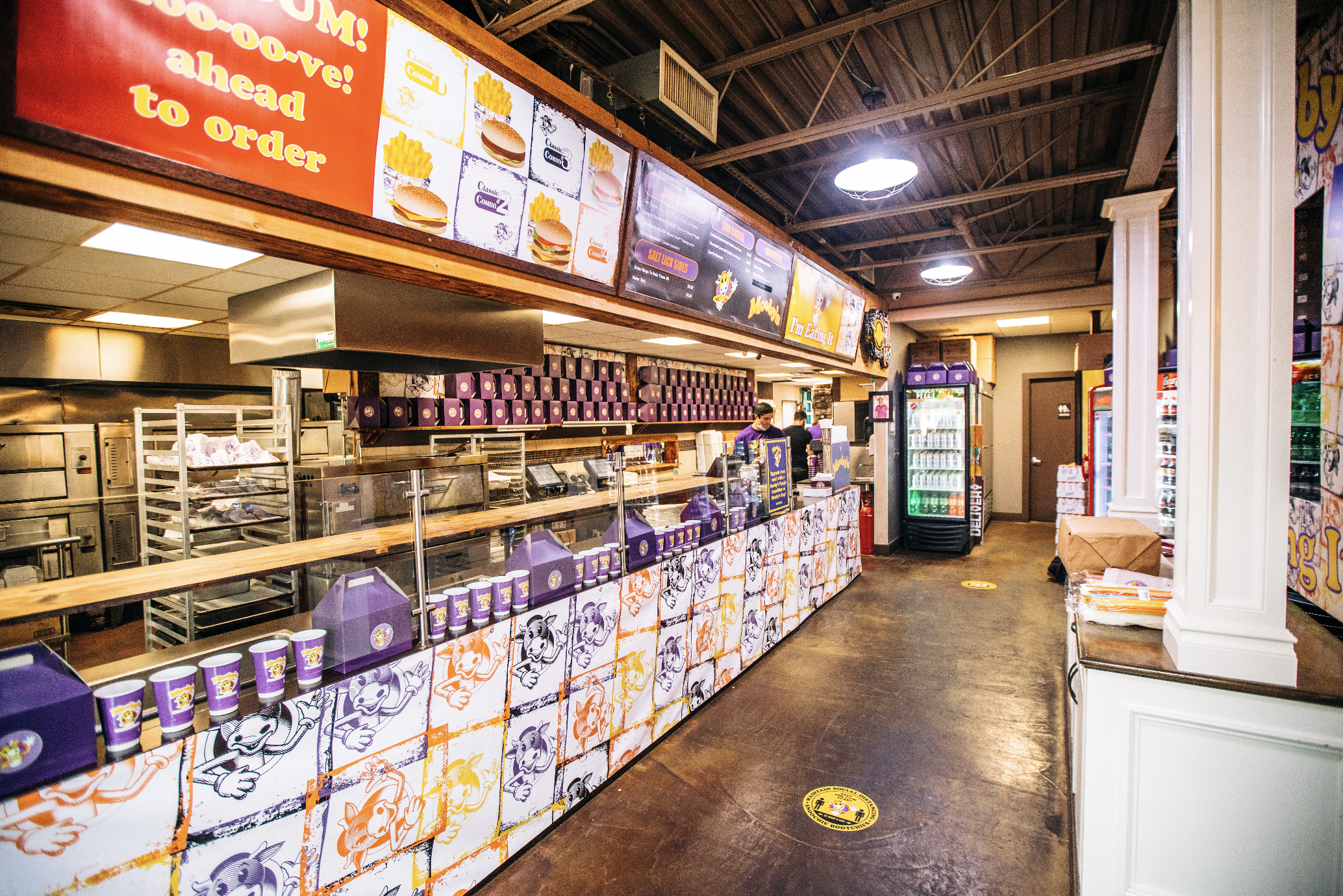 Wide view of the rebranded Mooby's kitchen, menu boards, decorated counter, and packaging