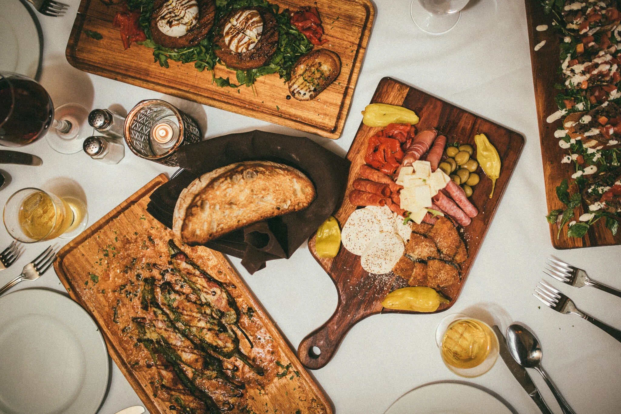 Overhead editorial photograph of Italian appetizers, charcuterie and bread spread across a restaurant table