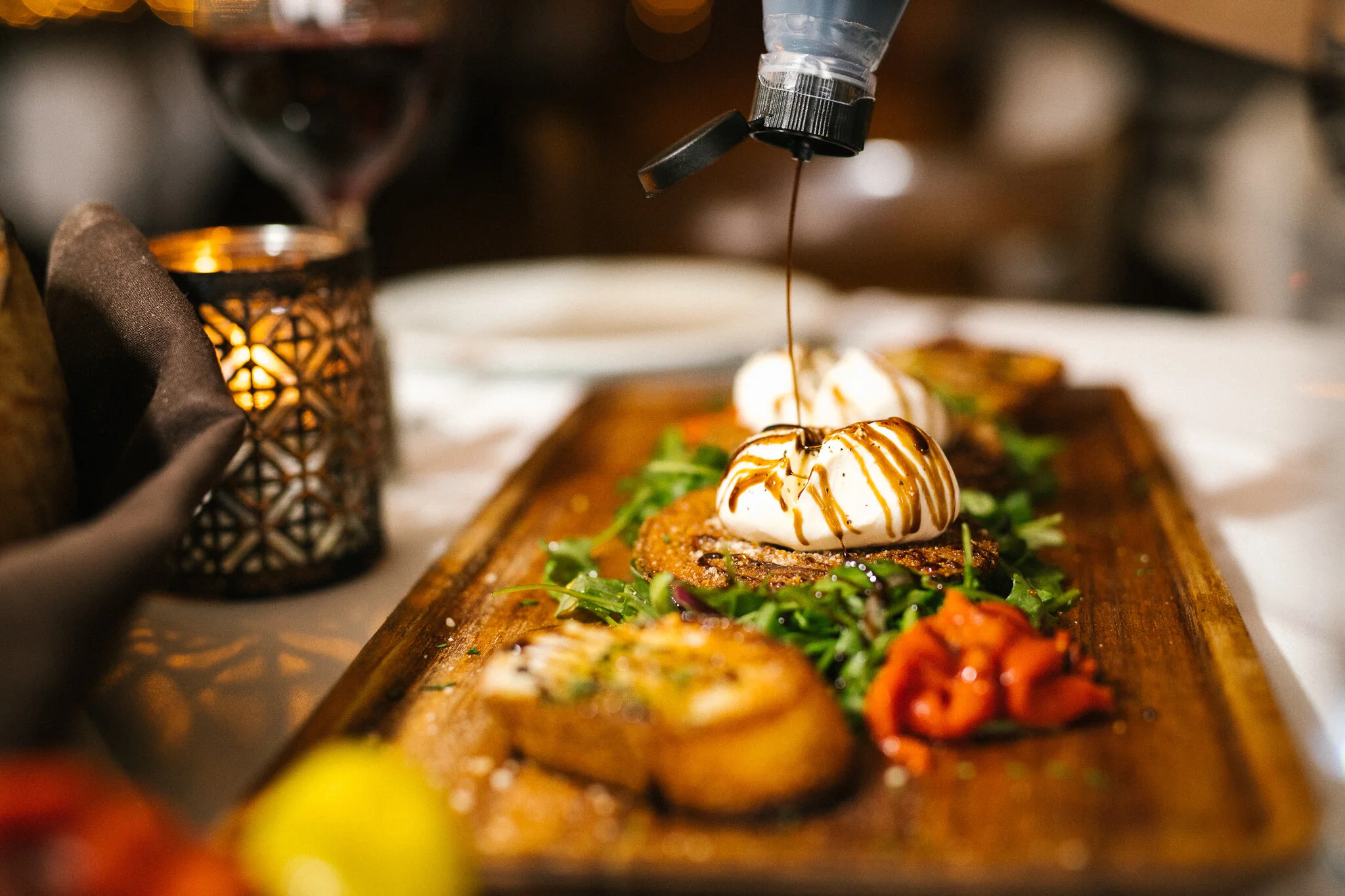 Balsamic glaze being drizzled over a restaurant appetizer on a wooden serving board