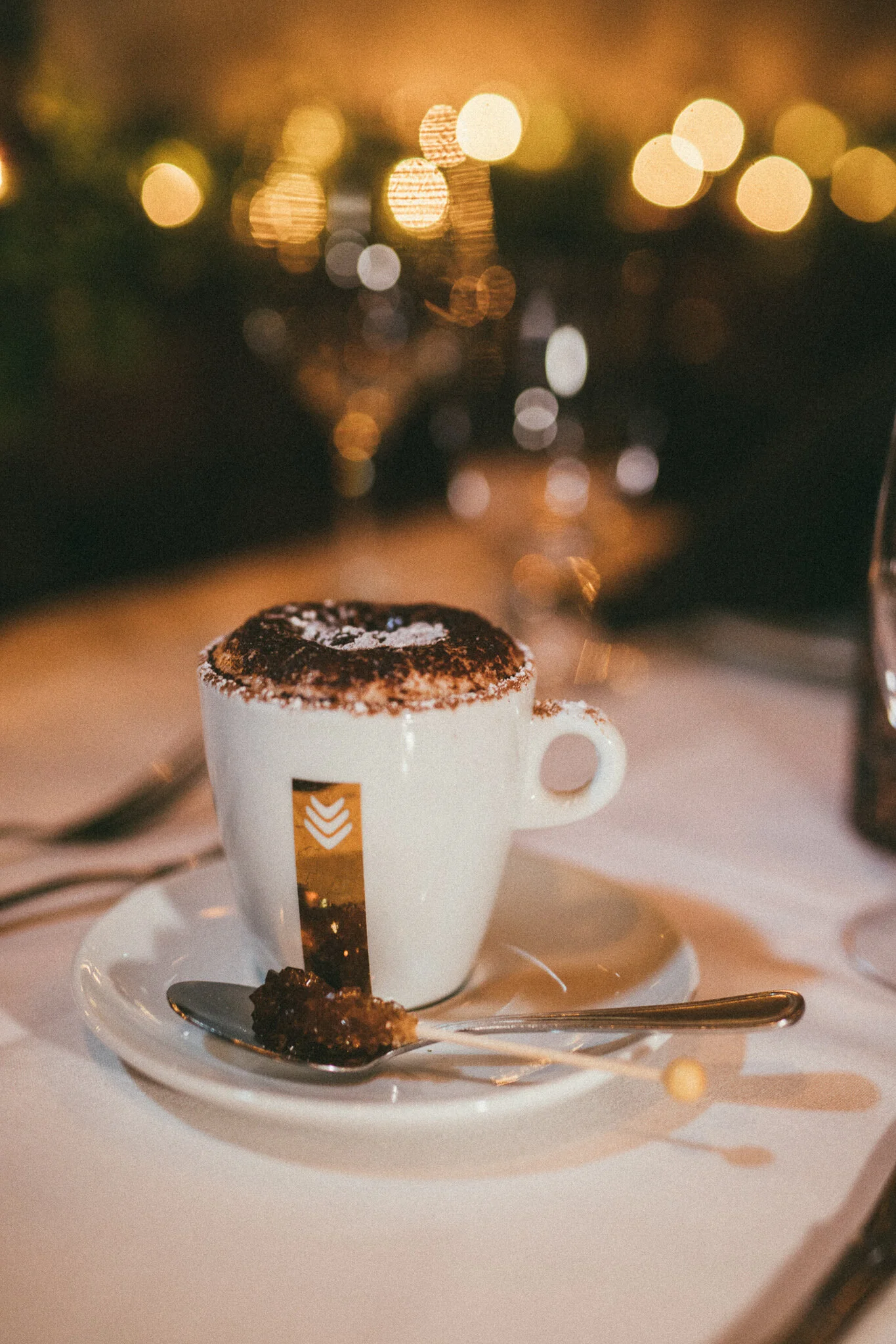 Close-up of a foamy Italian coffee in a white ceramic cup with golden bokeh in the background