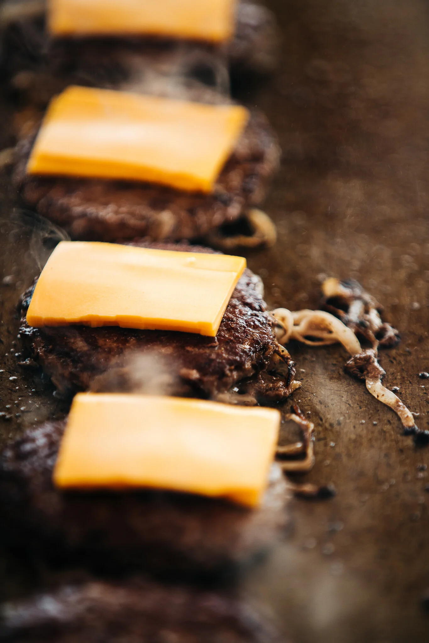 Close-up line of burger patties with melting American cheese on hot griddle