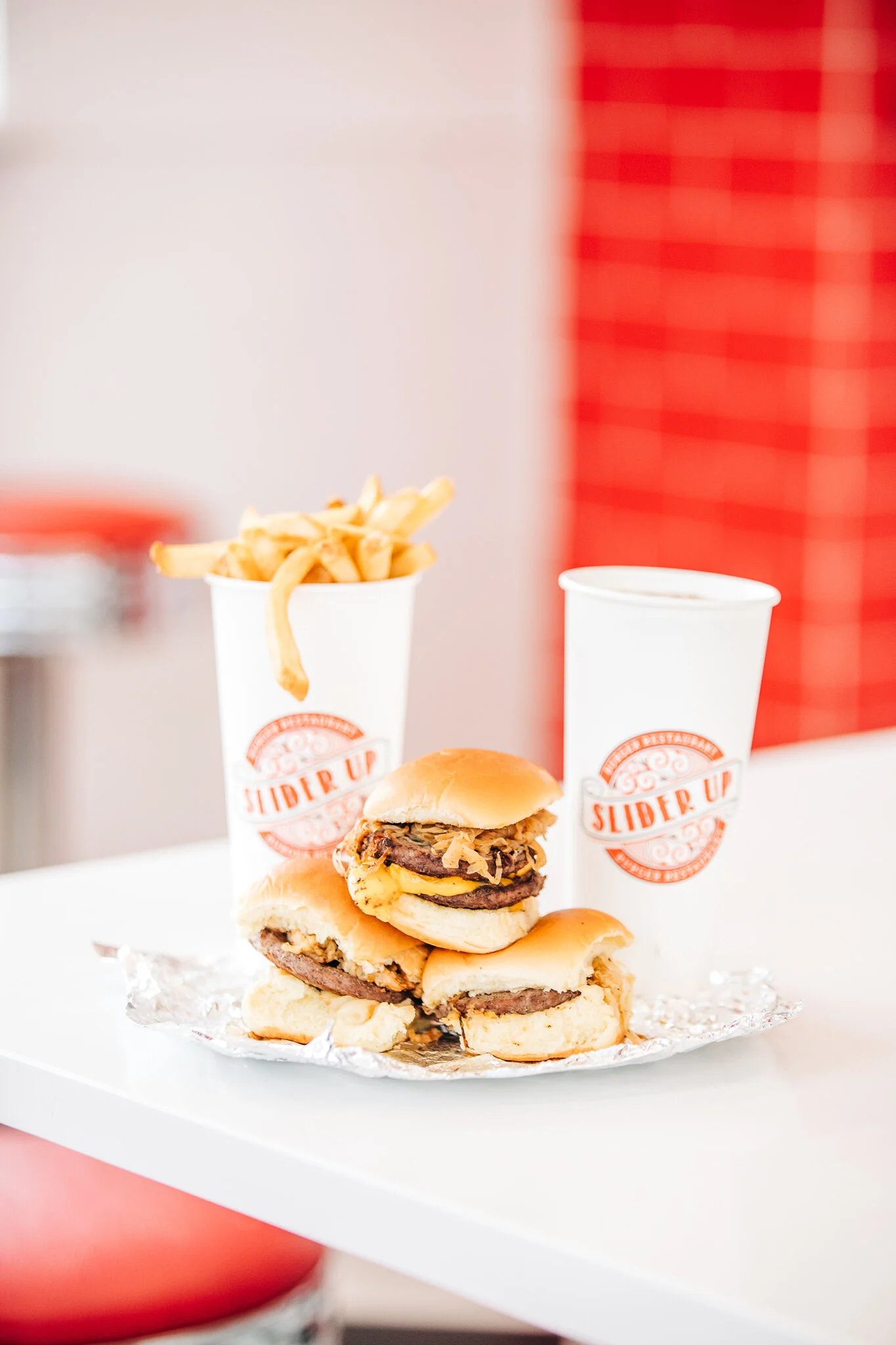 Three Slider Up burgers stacked with branded fries cup and branded soda cup in red diner interior