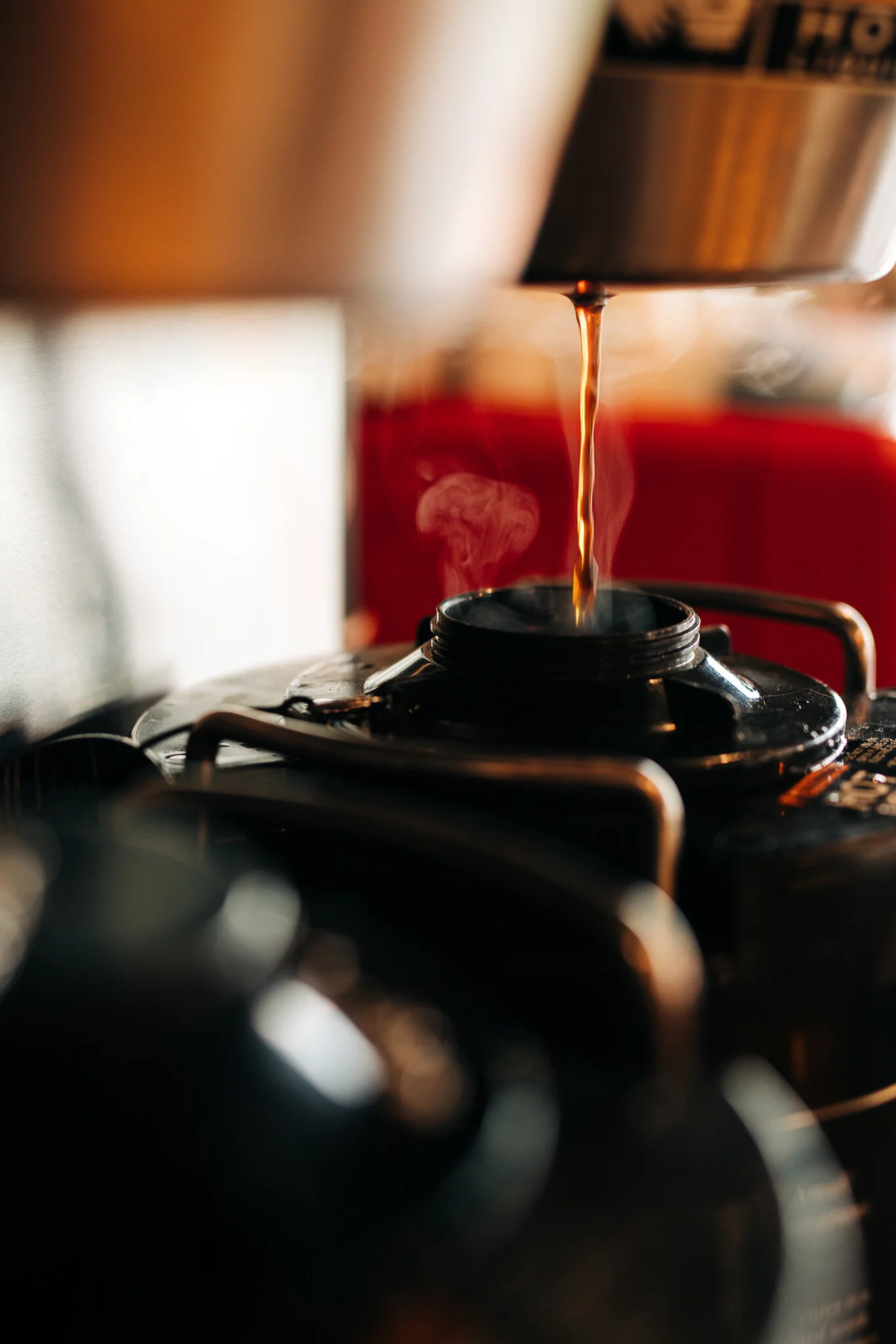 Close-up of hot coffee pouring into a thermal pot behind the counter