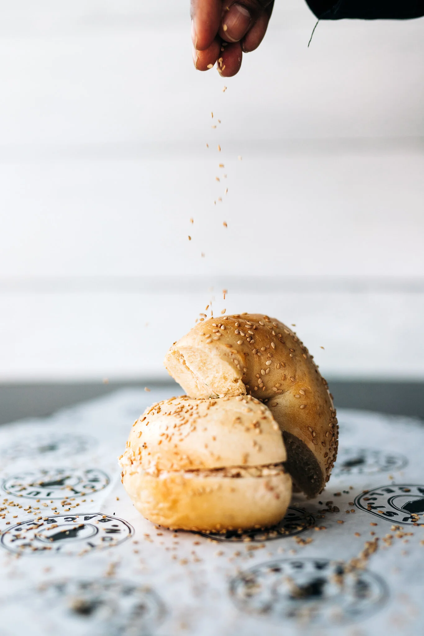 Sesame seeds falling onto fresh bagel sandwiches on Not Just Bagels branded wrapping paper