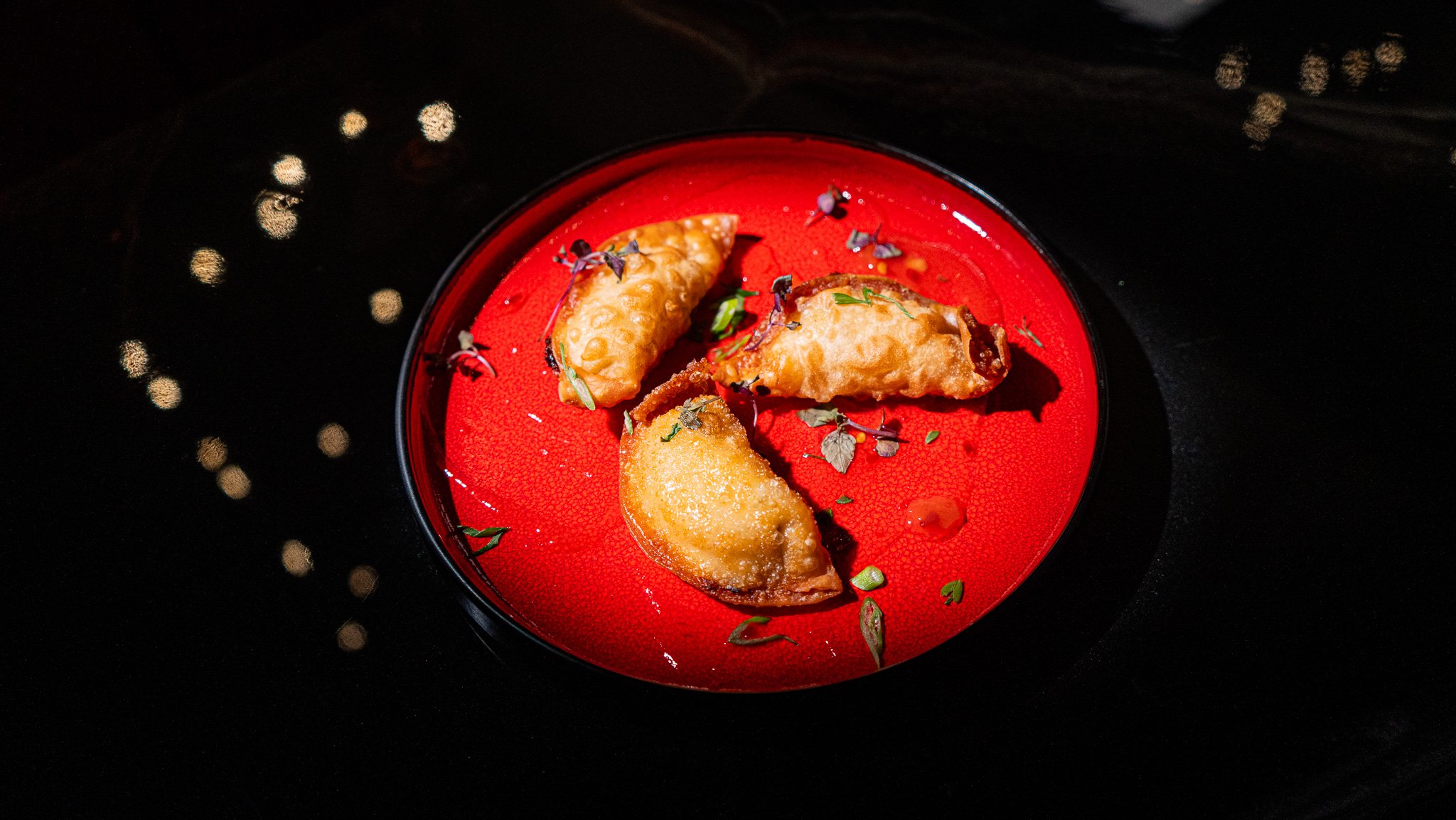 Three golden fried dumplings served on a vivid red plate against a dark table