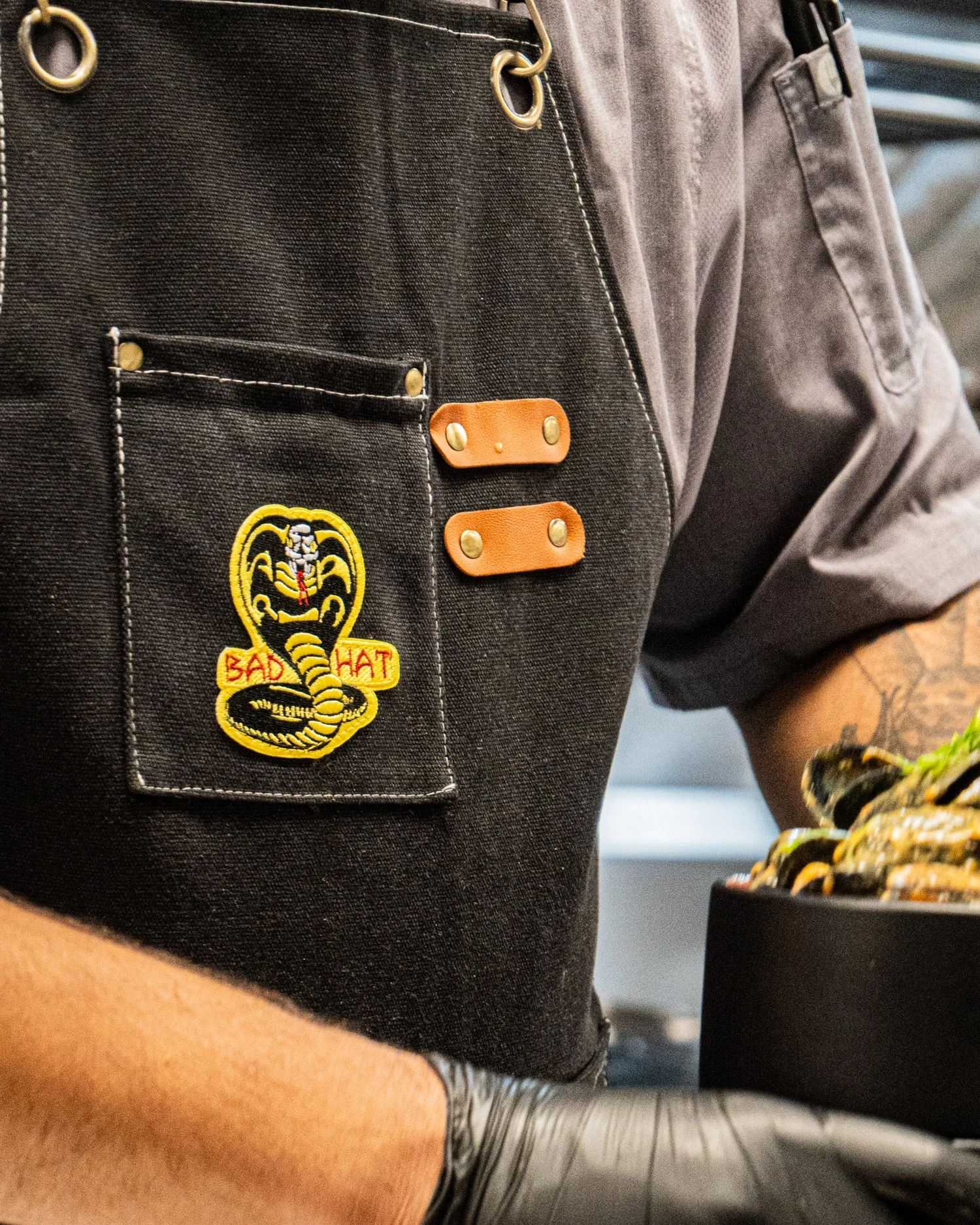 Close-up of the Bad Hat embroidered cobra emblem on a dark apron