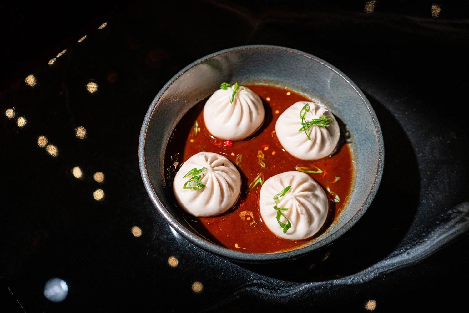 Dumplings served in a dark dish with a rich dipping sauce