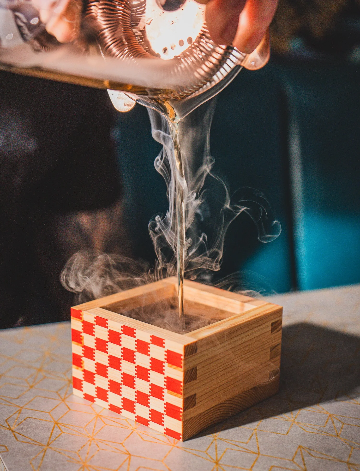 Cocktail being poured into a wooden presentation box with dramatic vapor
