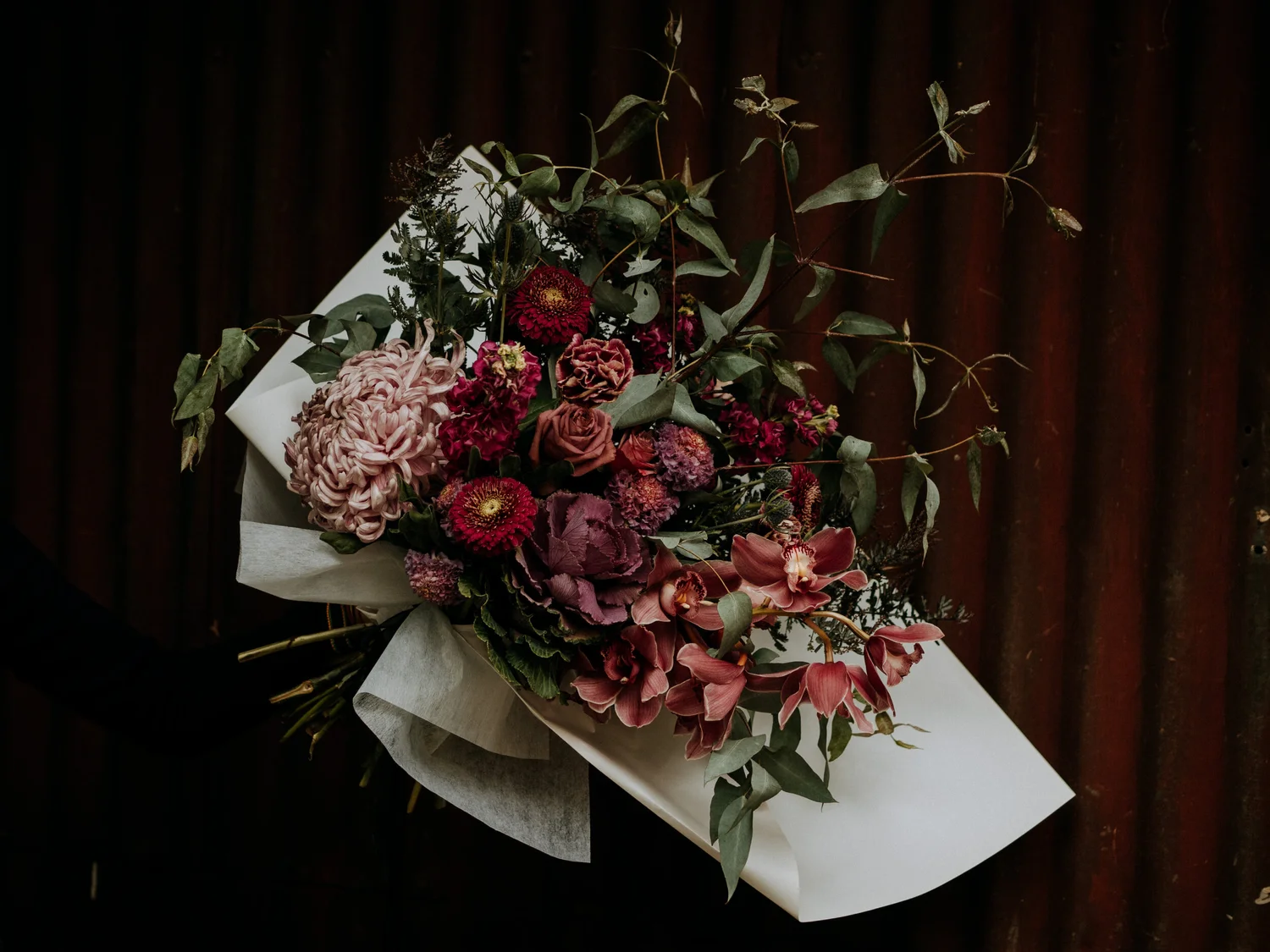 Moody Luna Moss bouquet of burgundy dahlias, orchids and eucalyptus wrapped in white paper