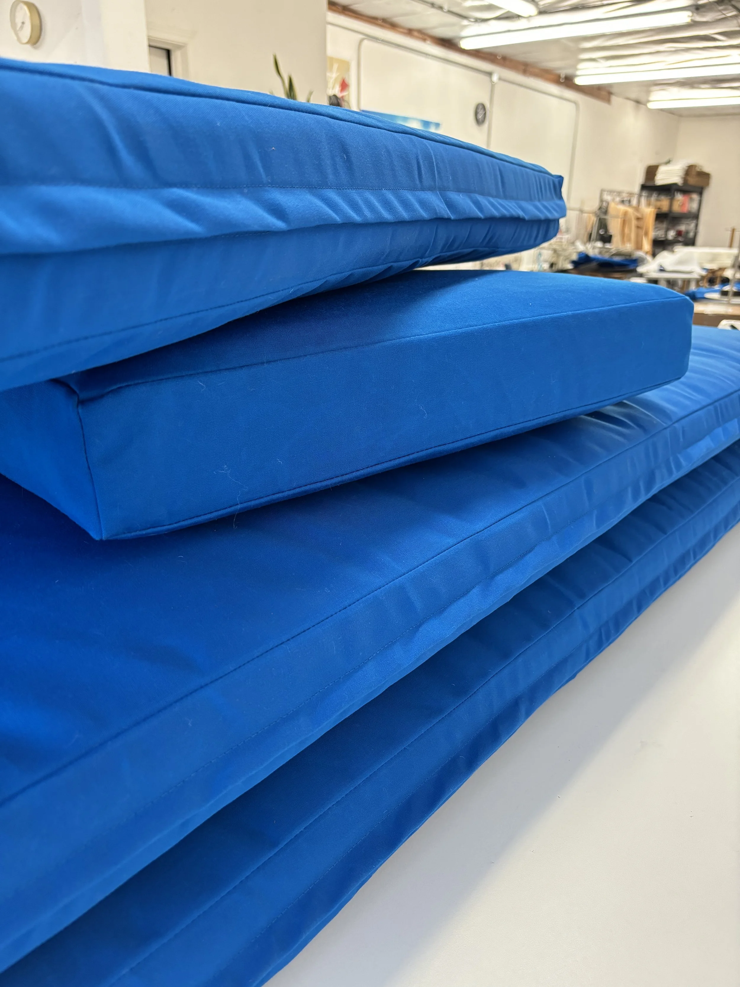 Close-up view of blue cushioned mattresses stacked on top of each other in a storage or warehouse room.