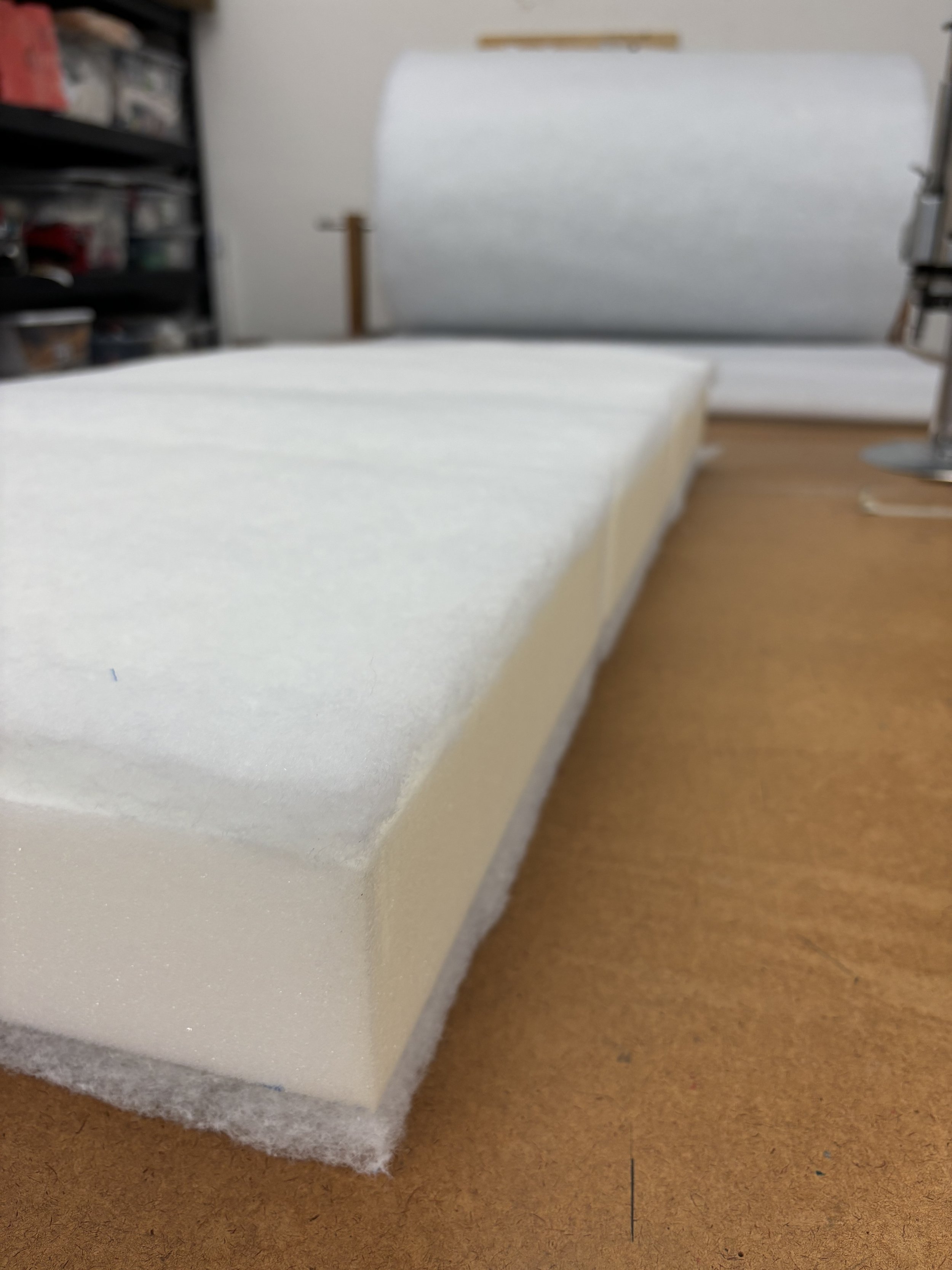 A close-up photo of a white foam block on a brown surface, with shelves filled with supplies in the background.