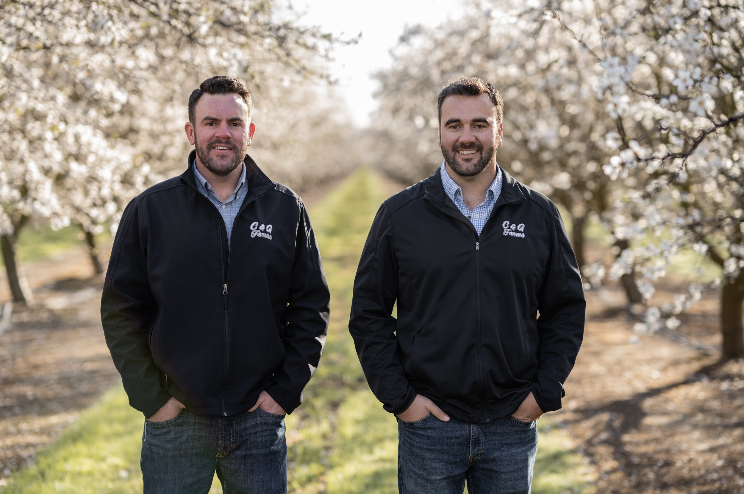 Two brothers who are third-generation farmers standing in an almond  orchard in bloom.