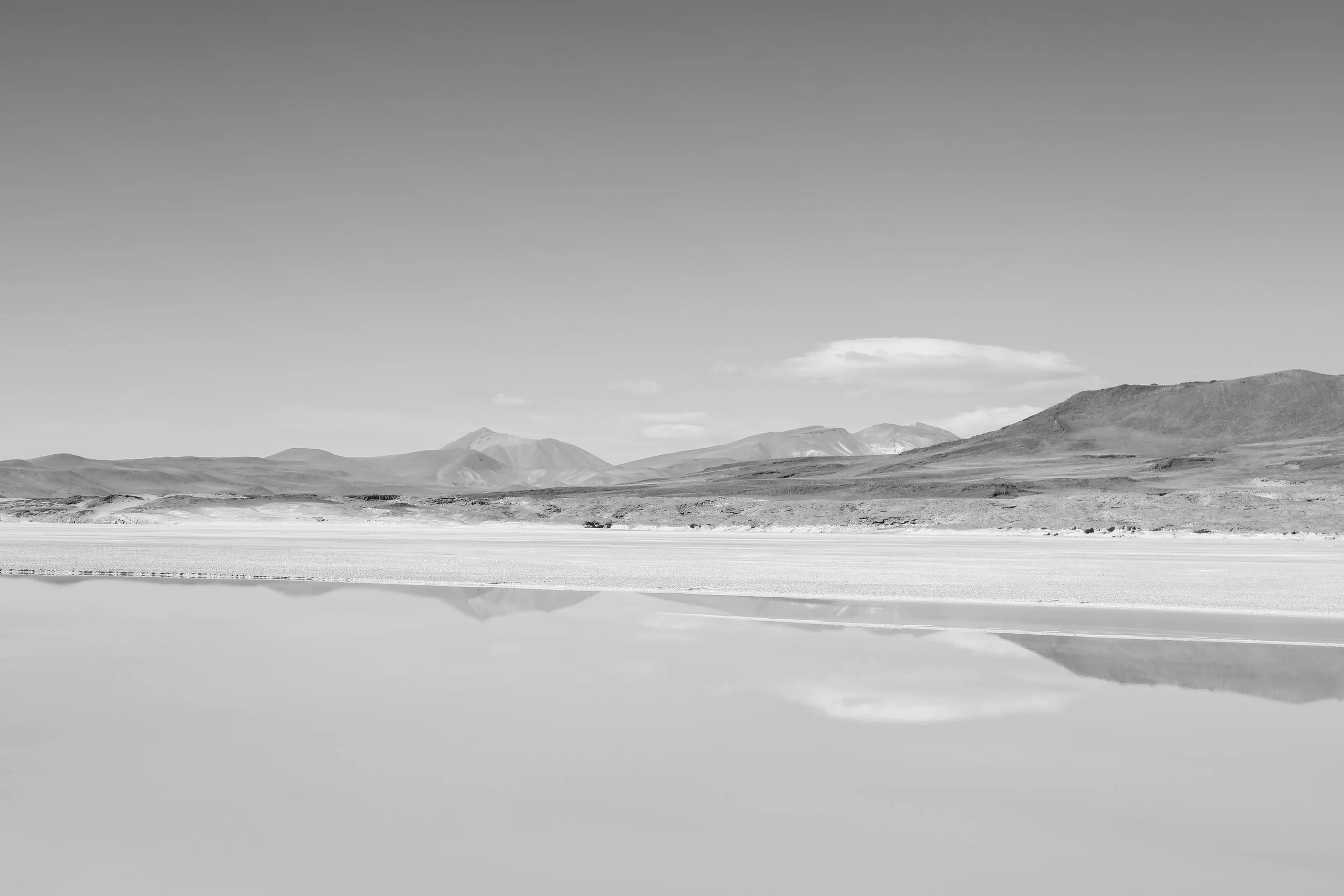Black and white landscape of mountains reflecting in a still lake with a clear sky.