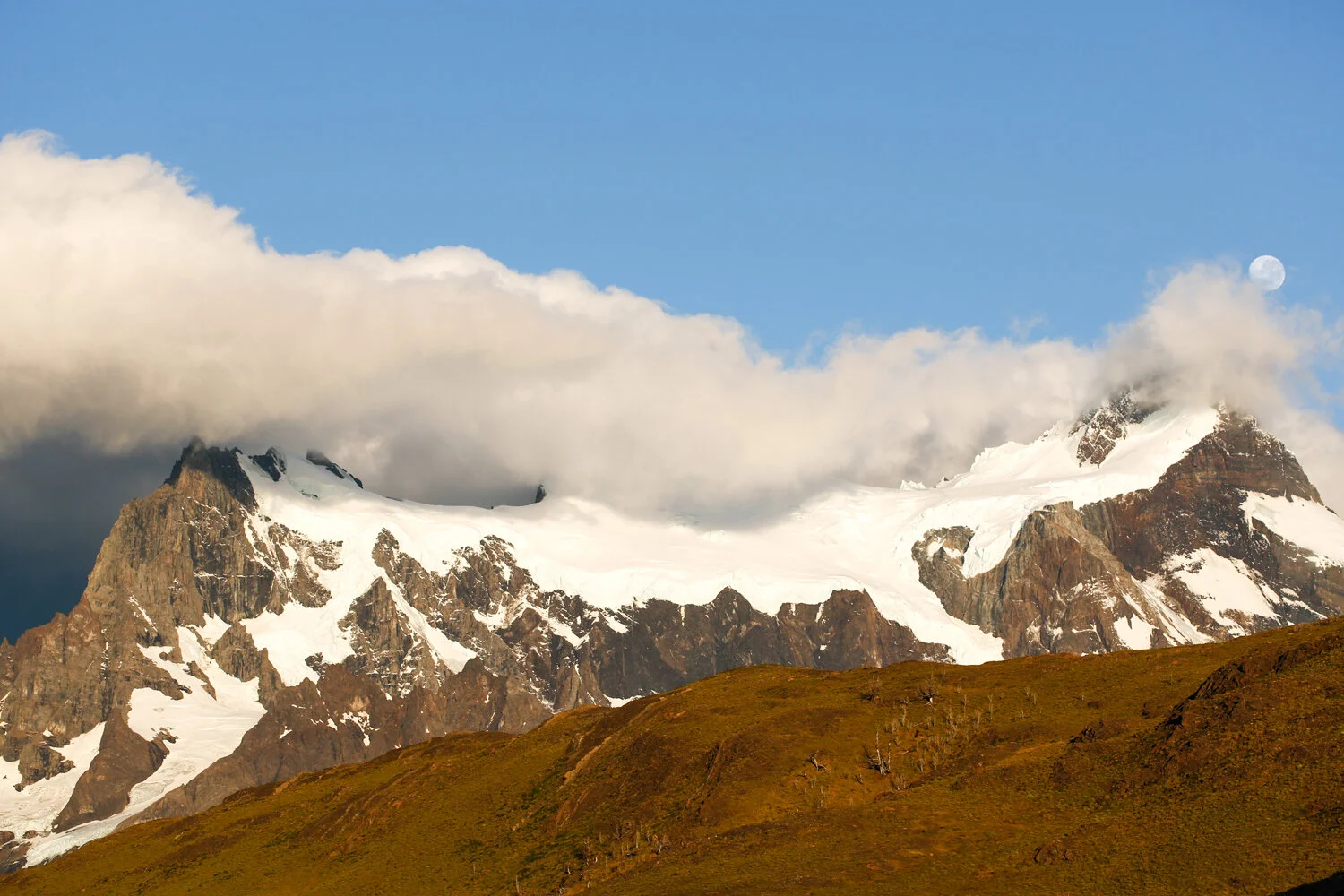 Snow-covered mountains with clouds and blue sky.