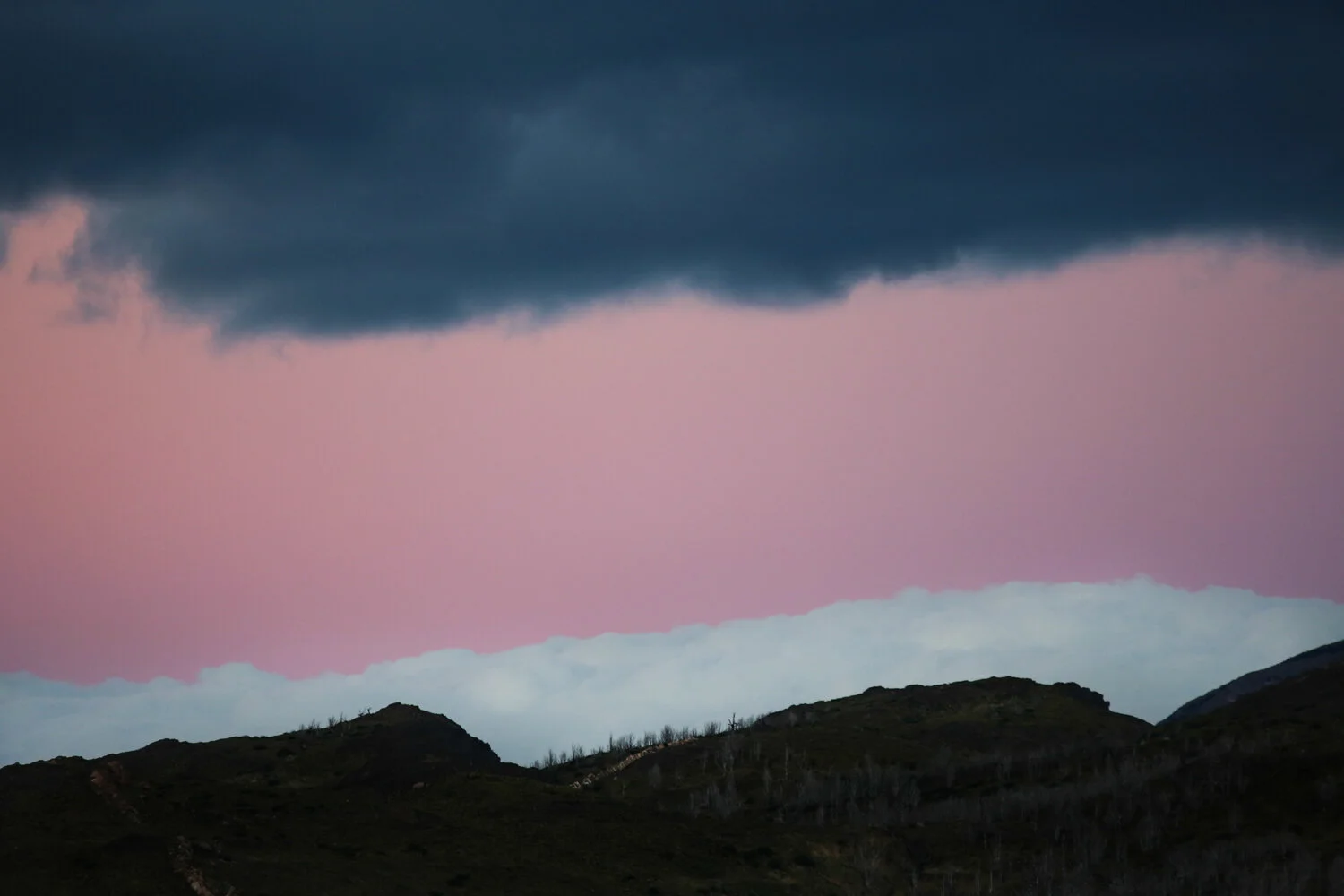 Dark storm clouds above a pink and gray sky with silhouetted hills.