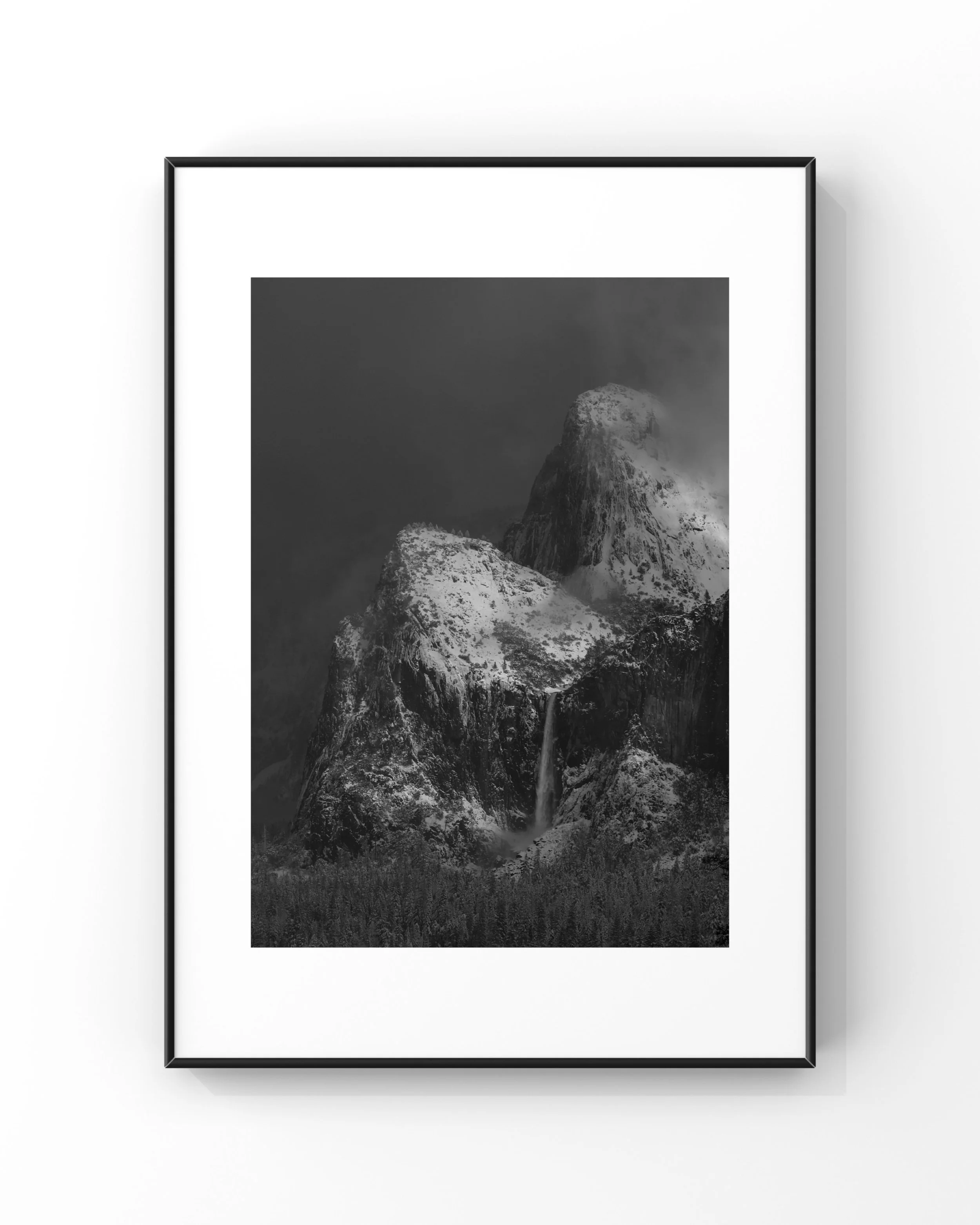 Black and white photograph of a snow-covered mountain with a waterfall, framed and hung on a wall.