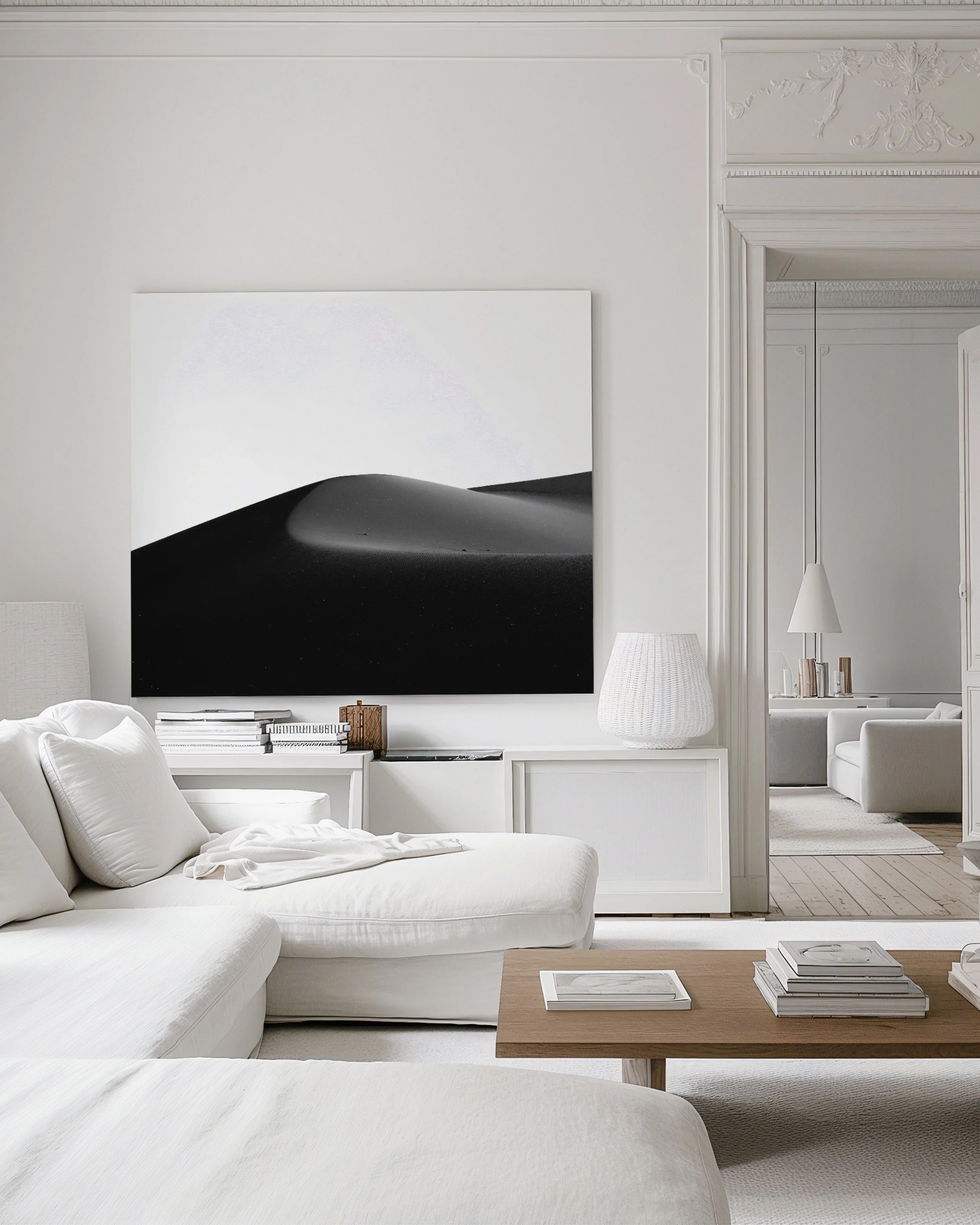 Minimalist living room with white sofas, black and white artwork of sand dunes, wooden coffee table, and neutral decor.
