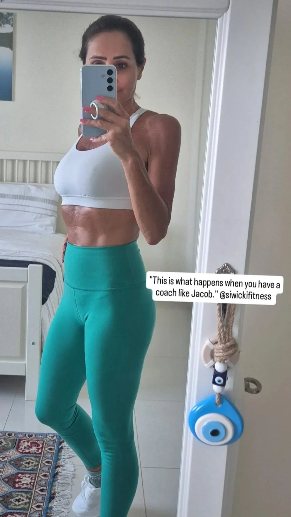 Woman taking a mirror selfie in black athletic attire with gold star decorations hanging on the side.