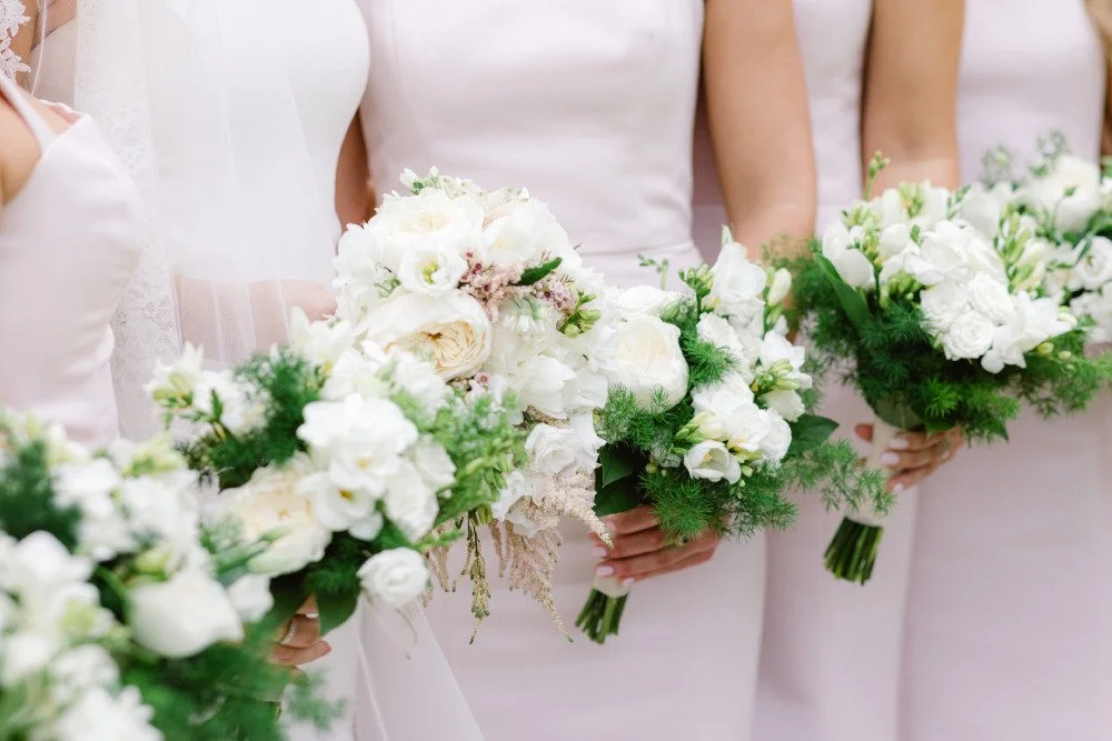 A close shot of a bride and her bridesmaids holding fresh white and green bouquets.