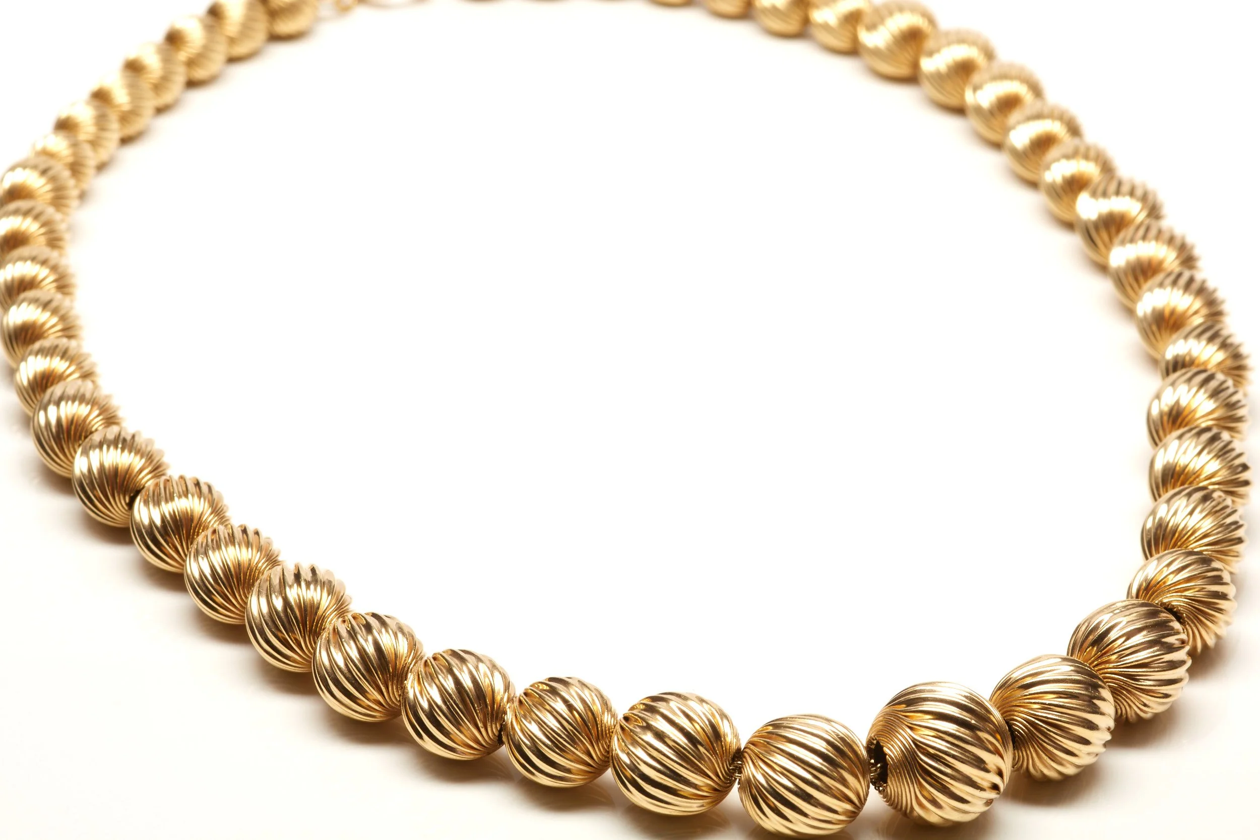 This Mid-Twentieth Century necklace is 15 1/2" long in 14-karat yellow gold and features twist-design, corrugated beads graduating from 6.5 to 12.5 mm


