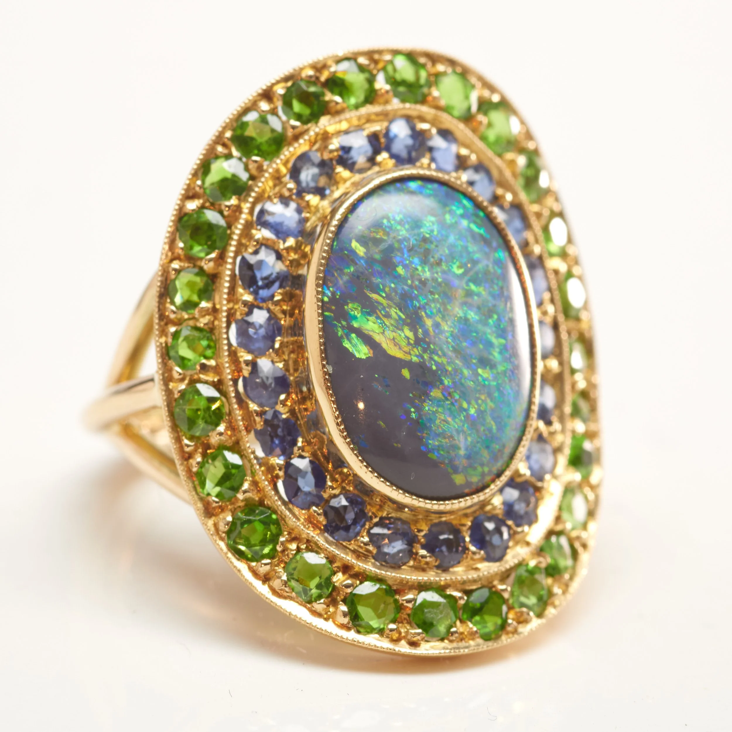 Antique rarity and vivid color in this Art Nouveau ring, set with a center black opal weighing about 2.50 carats surrounded by 21 sapphires  and 26 demantoid garnets. In 18-karat with 14-karat shank. Measures 1" x 3/4".