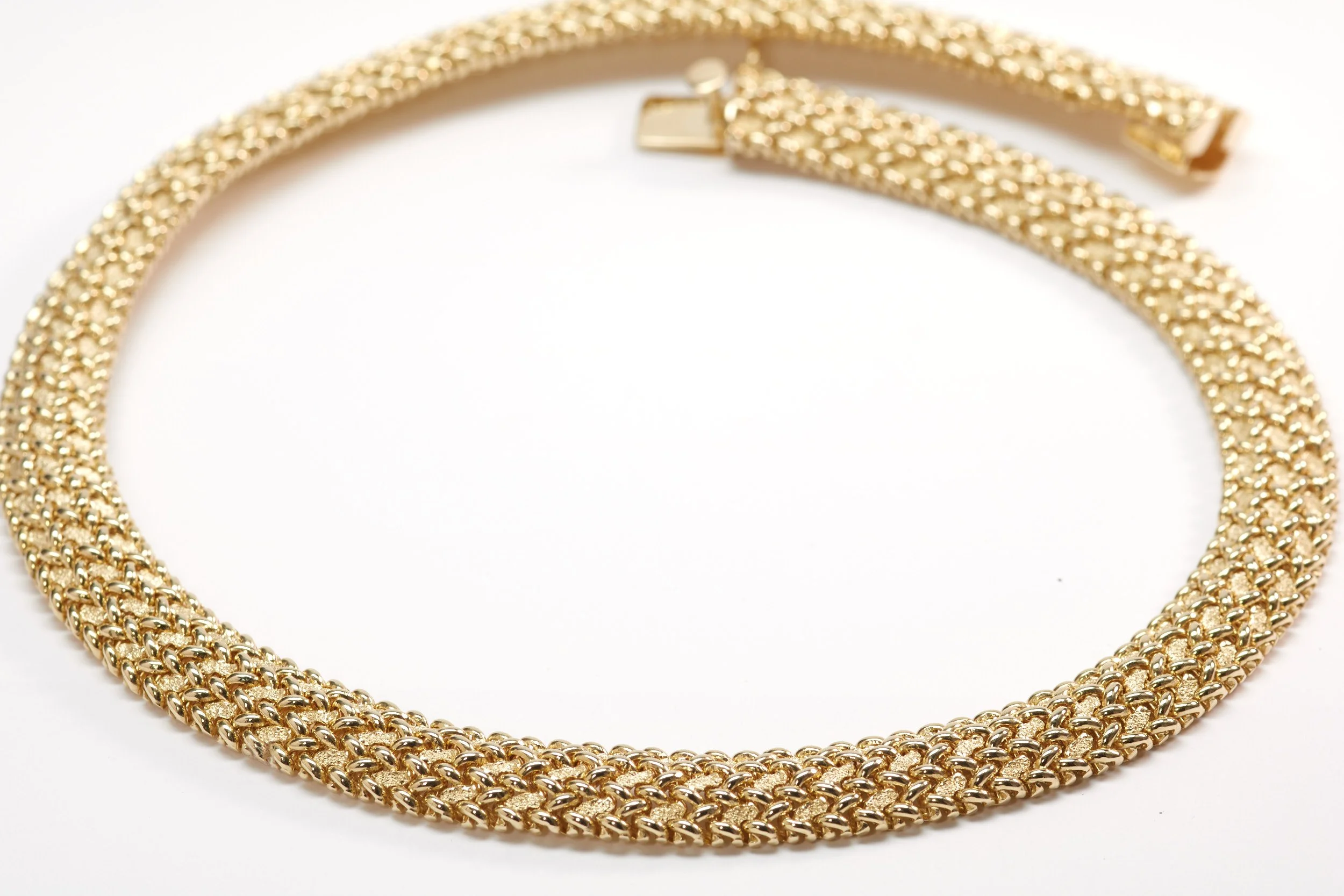A fascinating necklace in 14-karat yellow gold from the 1960s features high polished wires in a repeating "X" pattern on a textured background. Measures 3/8" wide and 16" long.
