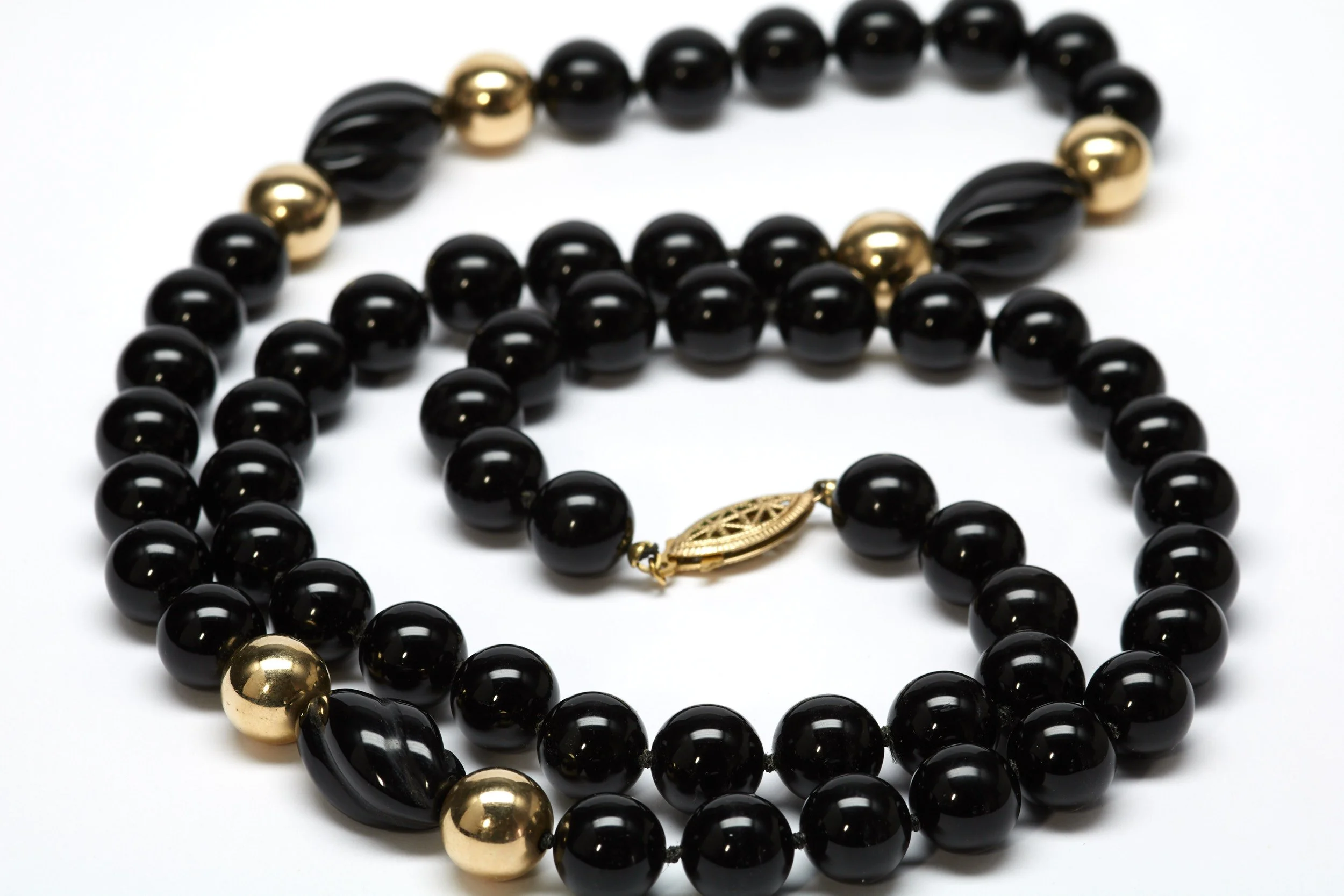 This necklace is clean of line with 54 round black onyx beads each measuring 10 mm, three more oblong and six more round in 14-karat yellow gold set. Measures 28" long.