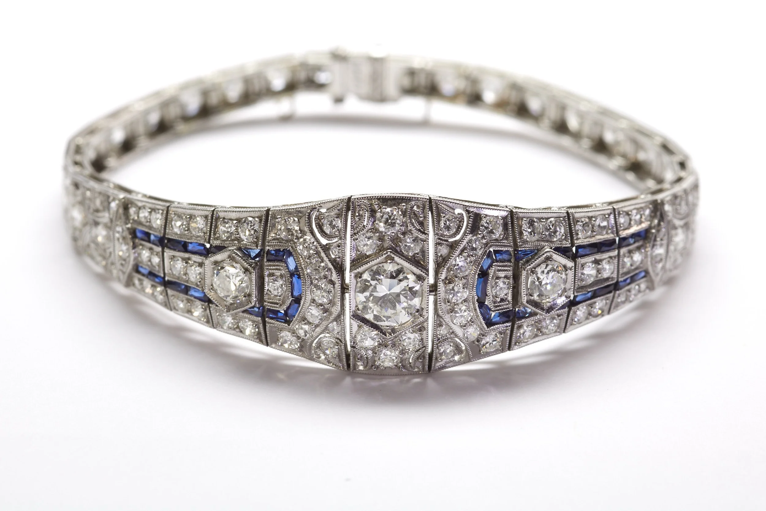 This brilliant Art Deco diamond bracelet has the classic elements of strong geometrical design, outstanding hand workmanship with milgrain detail, and bold colored stone accents in synthetic blue sapphires. It is mounted with 114 diamonds weighing ab