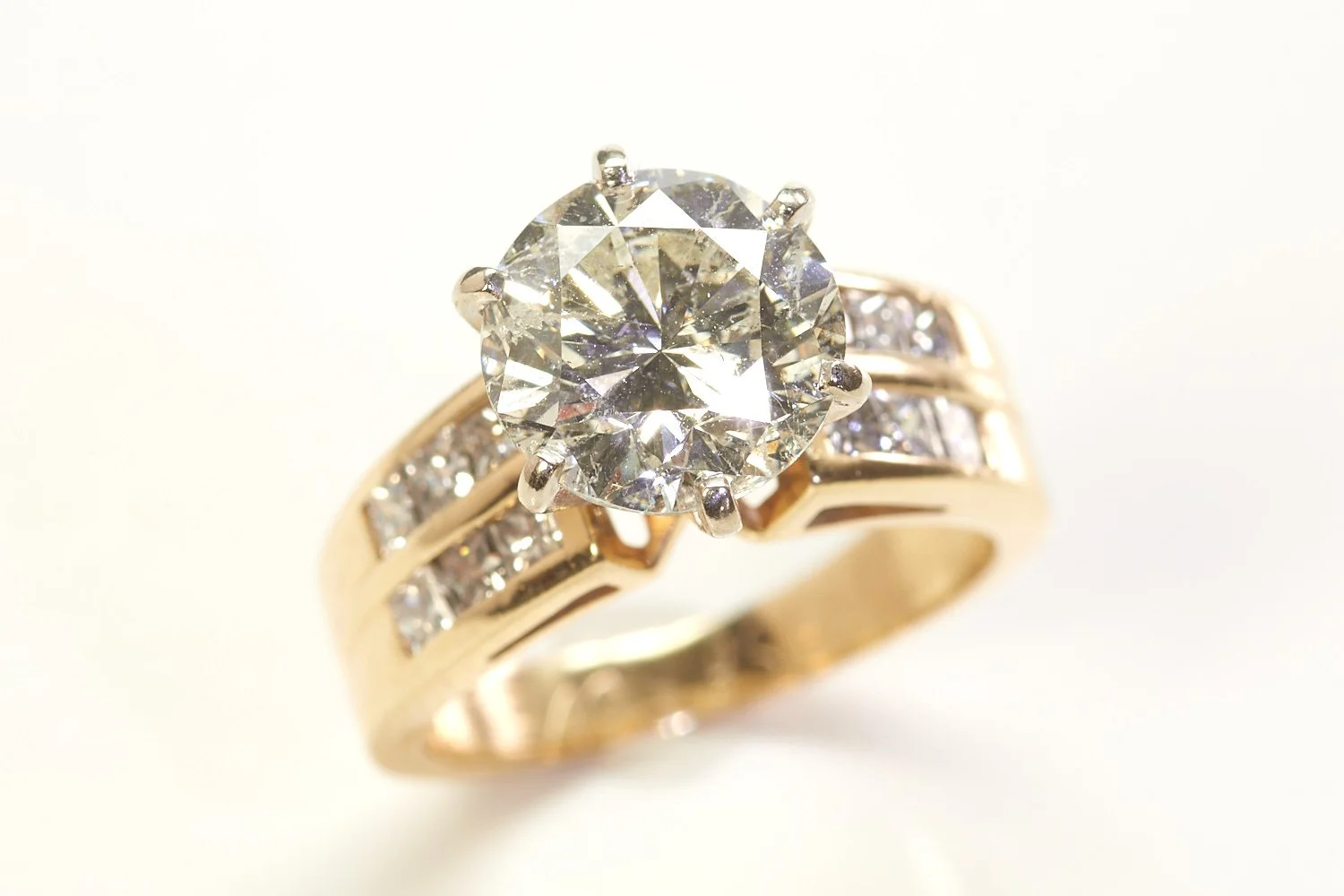 14-karat yellow gold engagement ring set with a round brilliant cut diamond weighing 4.06 carats and smaller princess-cut diamonds below.