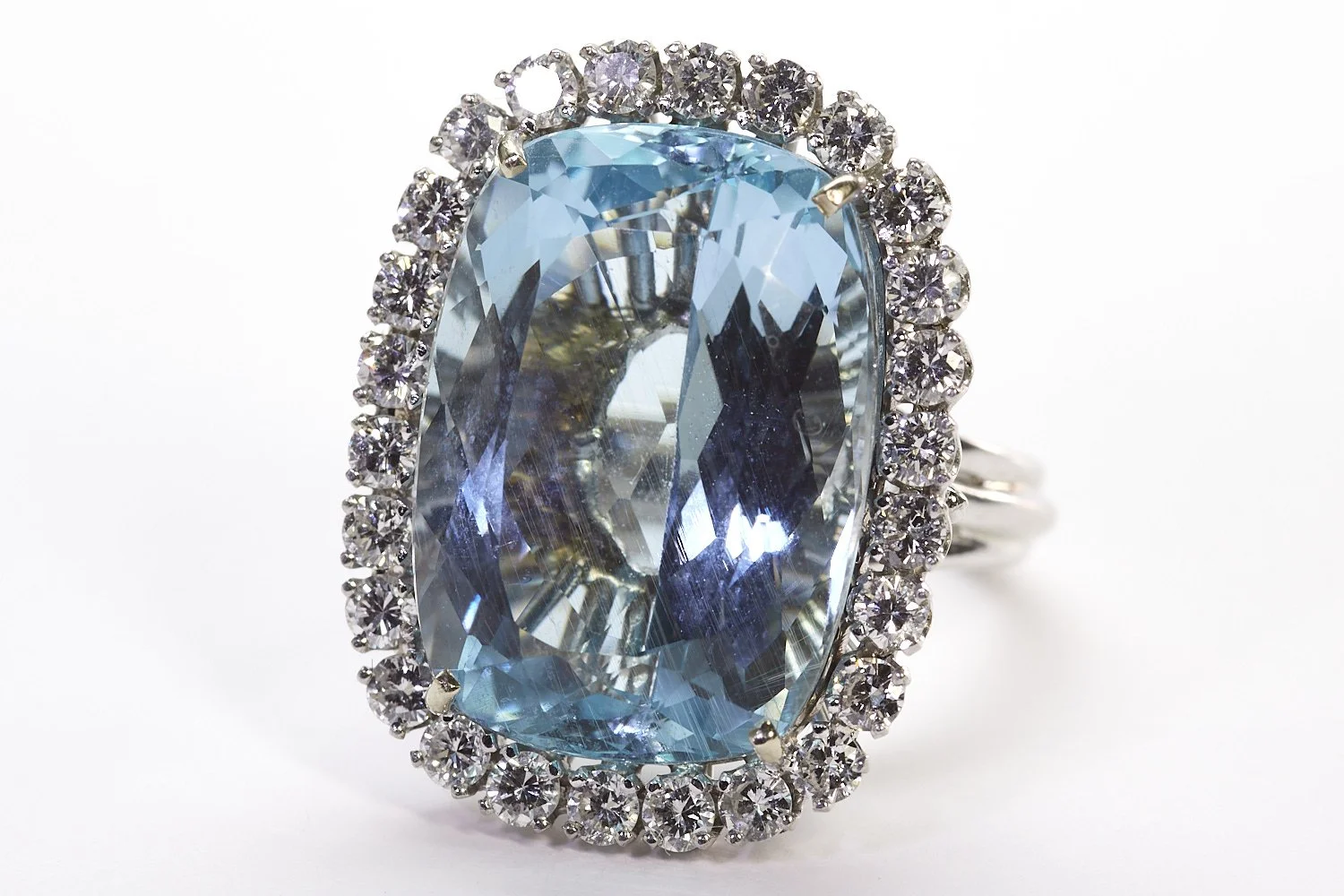 A hand-made ring in 14-karat white gold, featuring an approximately 22 carat cushion-shaped 
aquamarine surrounded by twenty-six diamonds weighing about 2.00 carats total. 