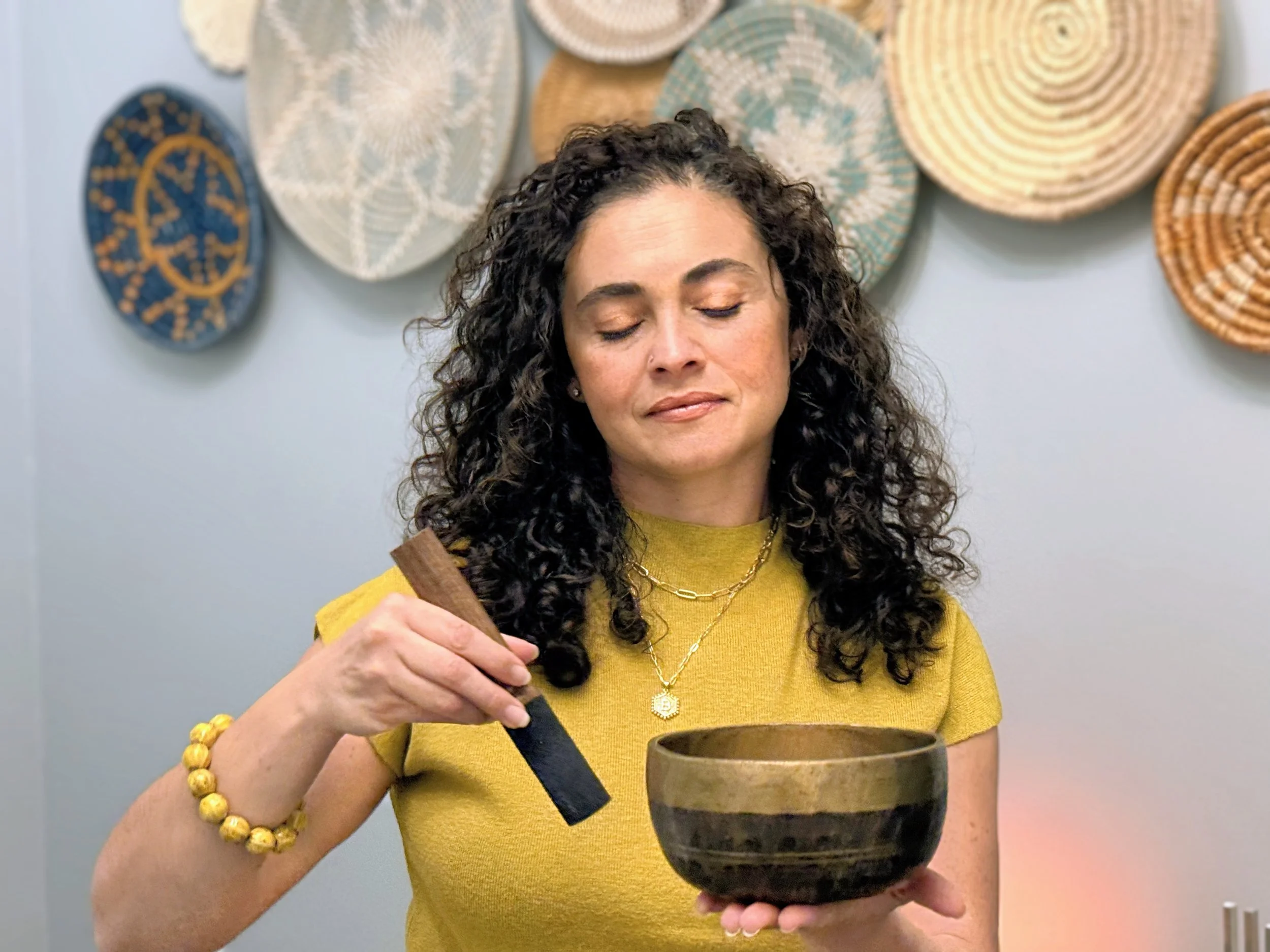 Curly haired woman plays a Himalayan singing bowl with a soft relaxed gaze.
