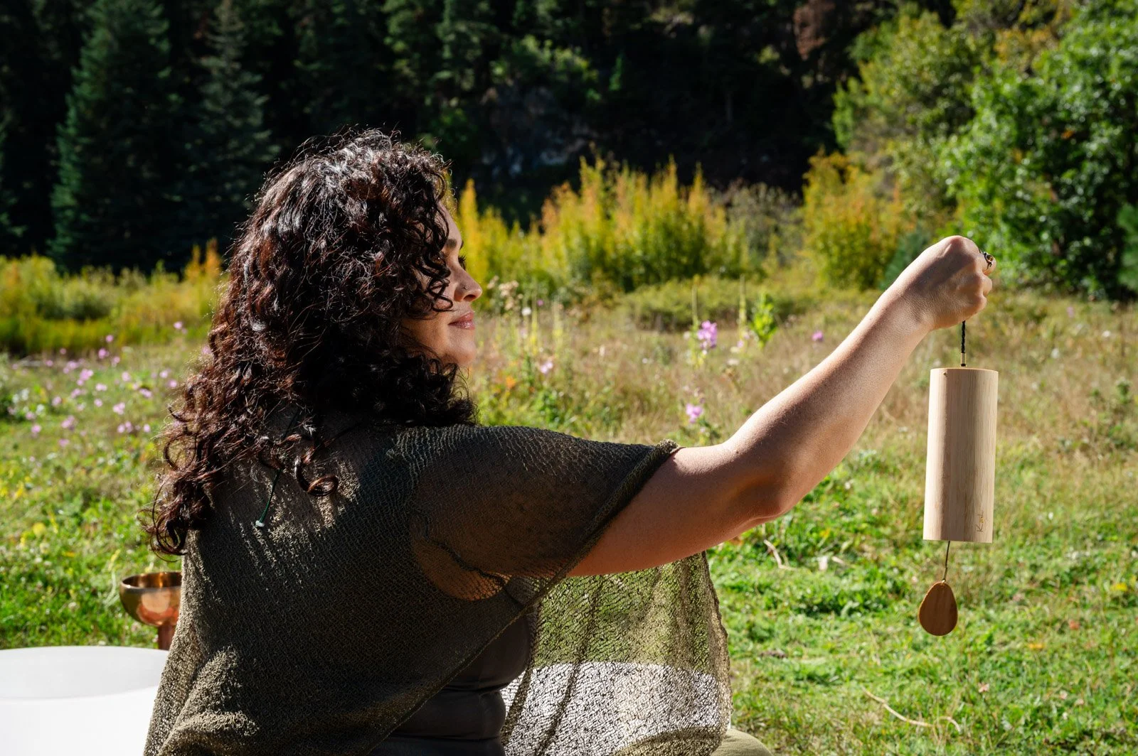 Natural setting with green grass and a woman holding a wind chime.