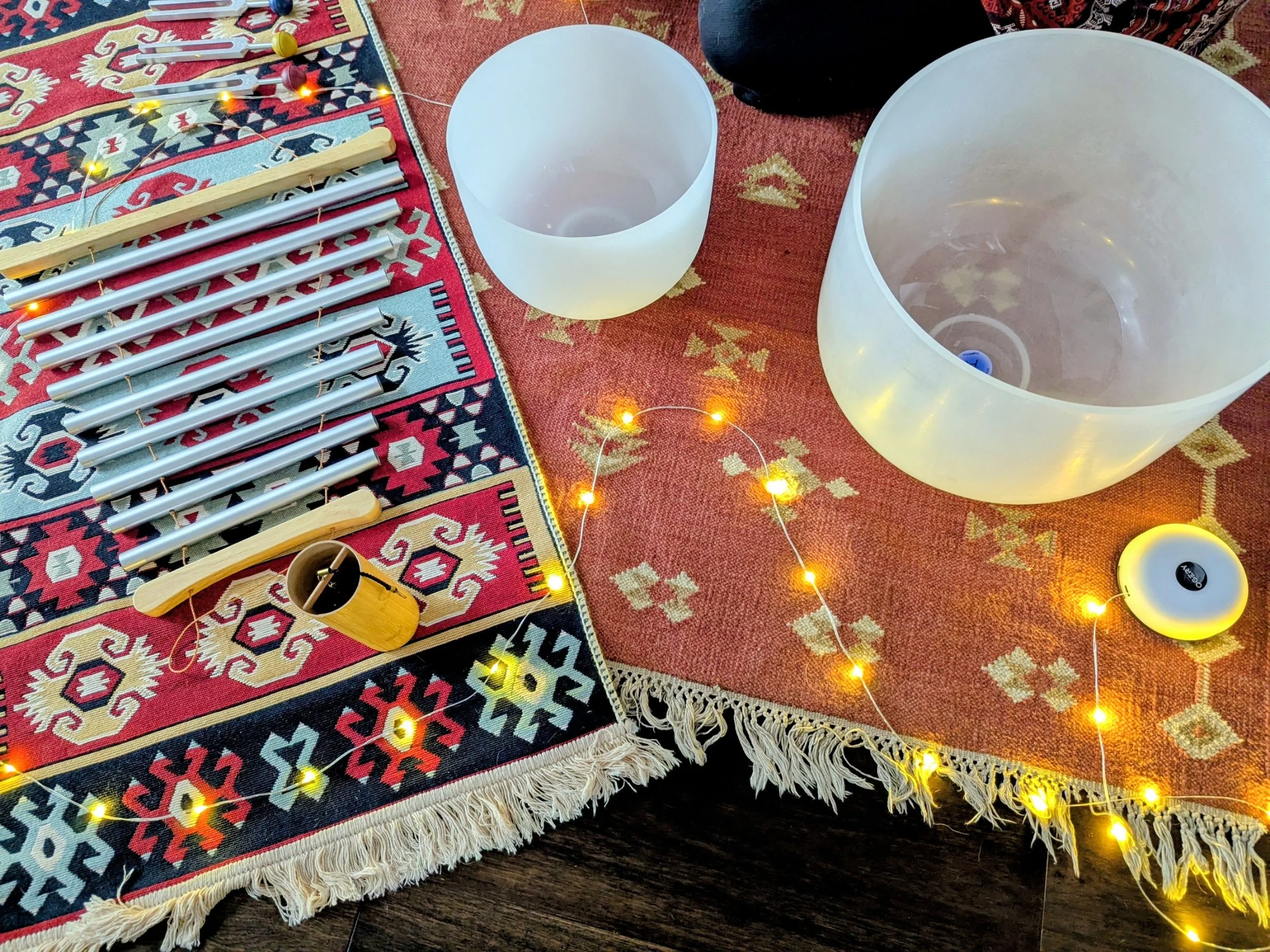 A decorative wooden table featuring a black singing bowl with an engraved symbol, a jar of white candle, a bunch of purple dried lavender, and a small potted plant in a metallic holder.