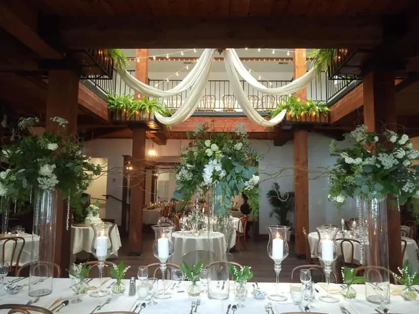 Elegant wedding reception with tall floral centerpieces, white tablecloths, and hanging drapery from the balcony ceiling.