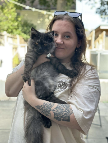 A girl with brown hair, wearing a cream t-shirt holds a cat up to her face for a cute picture.