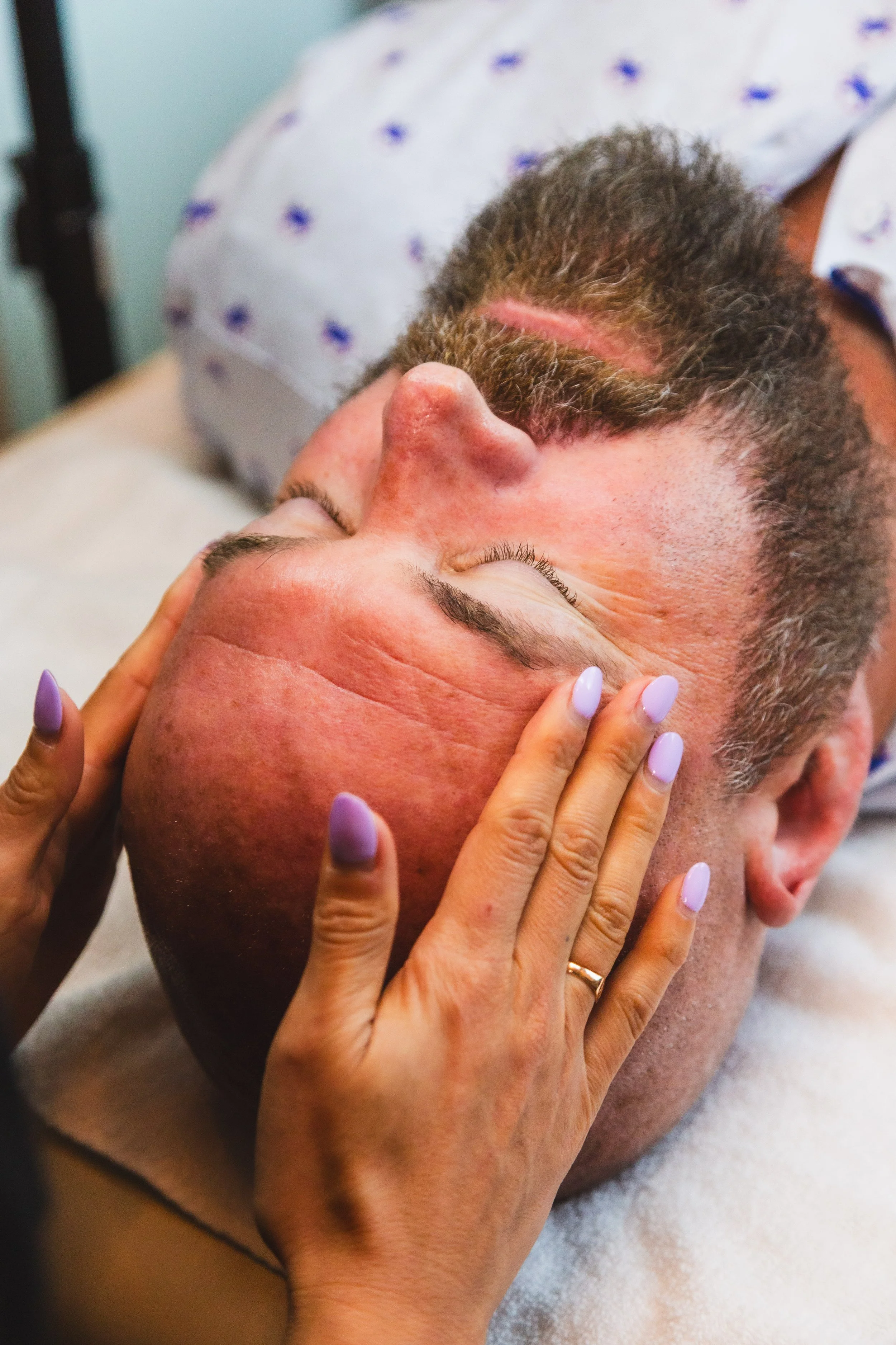 A man receiving a facial with his eyes closed, laying down.