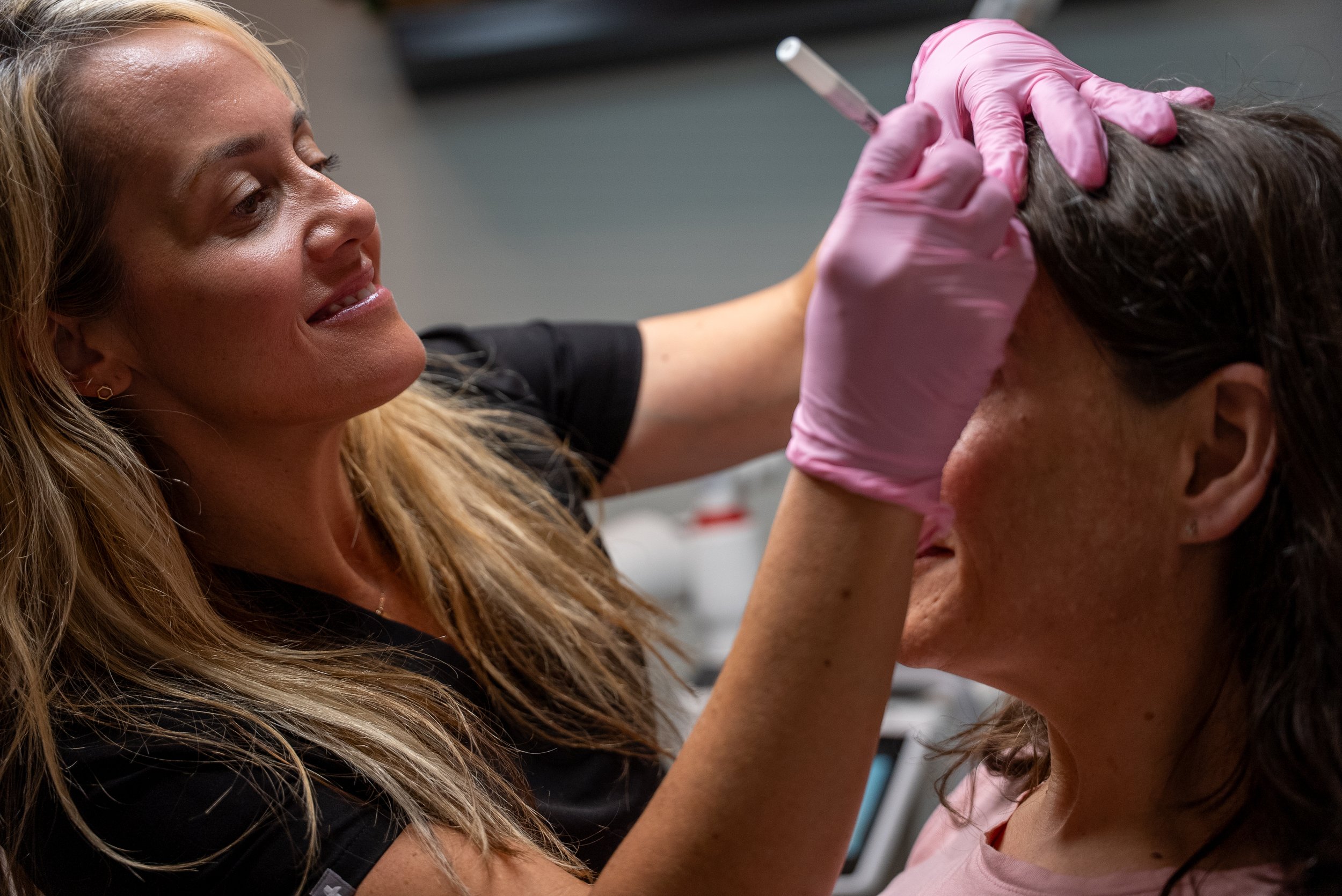 A woman receiving a cosmetic injection from a professional wearing pink gloves in a clinic setting.