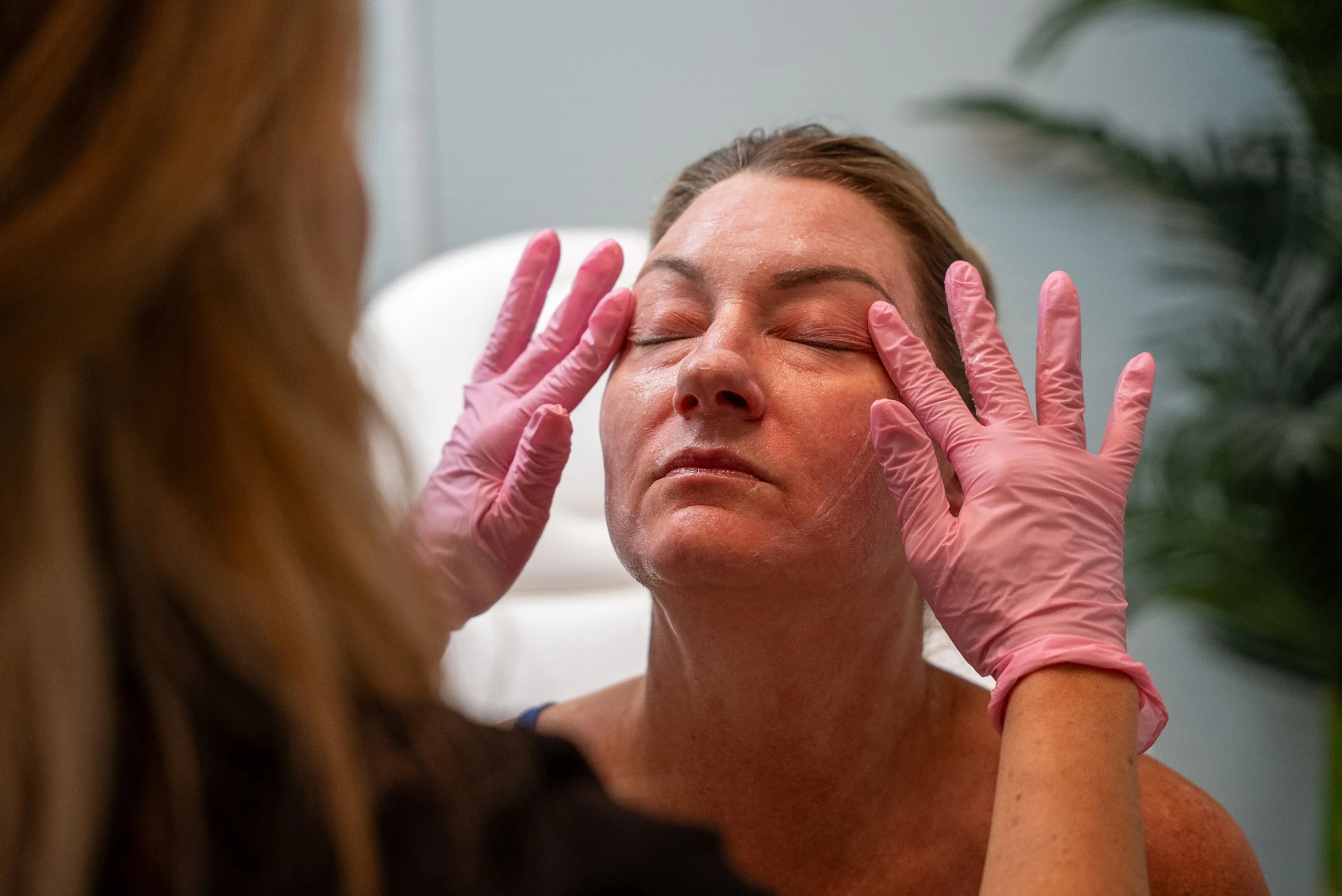 Licensed esthetician in pink gloves gently performing a professional facial massage on relaxed client during skincare treatment.