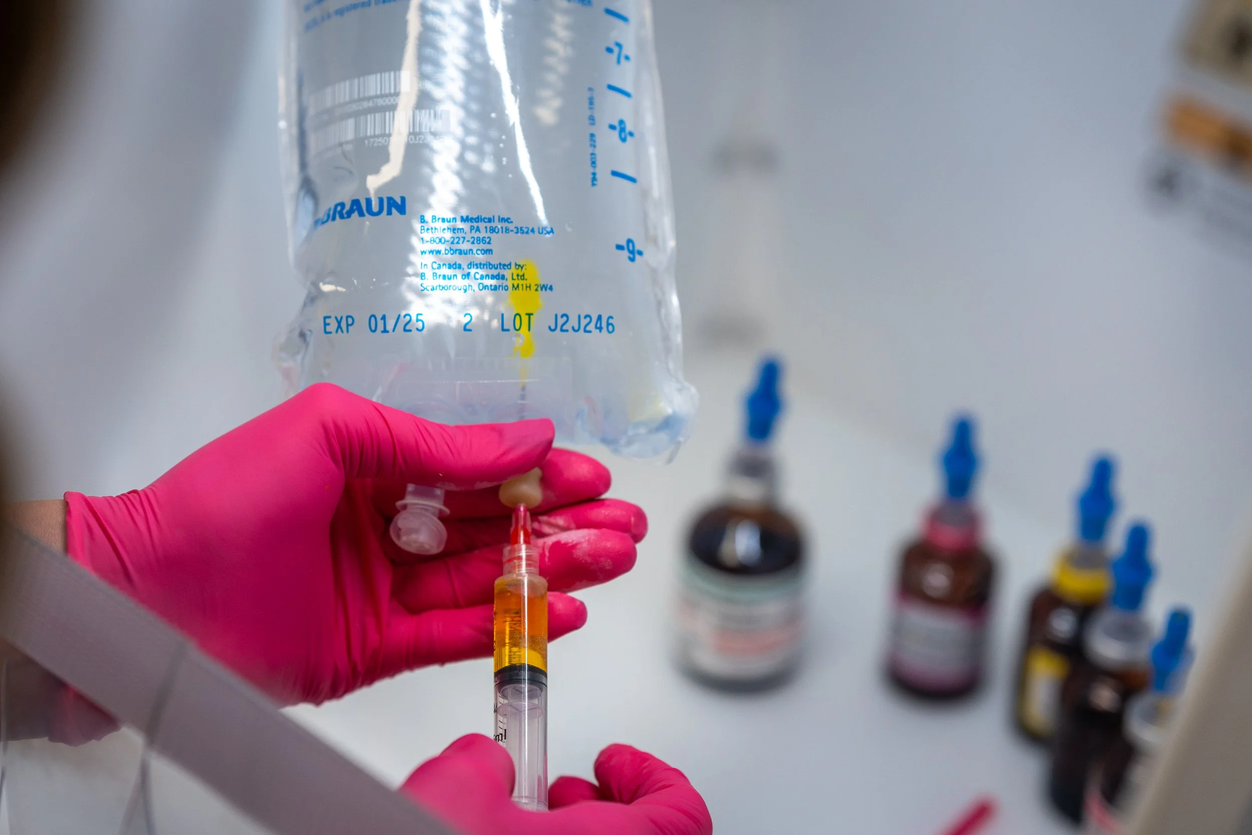 Medical professional in pink gloves preparing IV therapy treatment with vitamin solution in clinical setting.