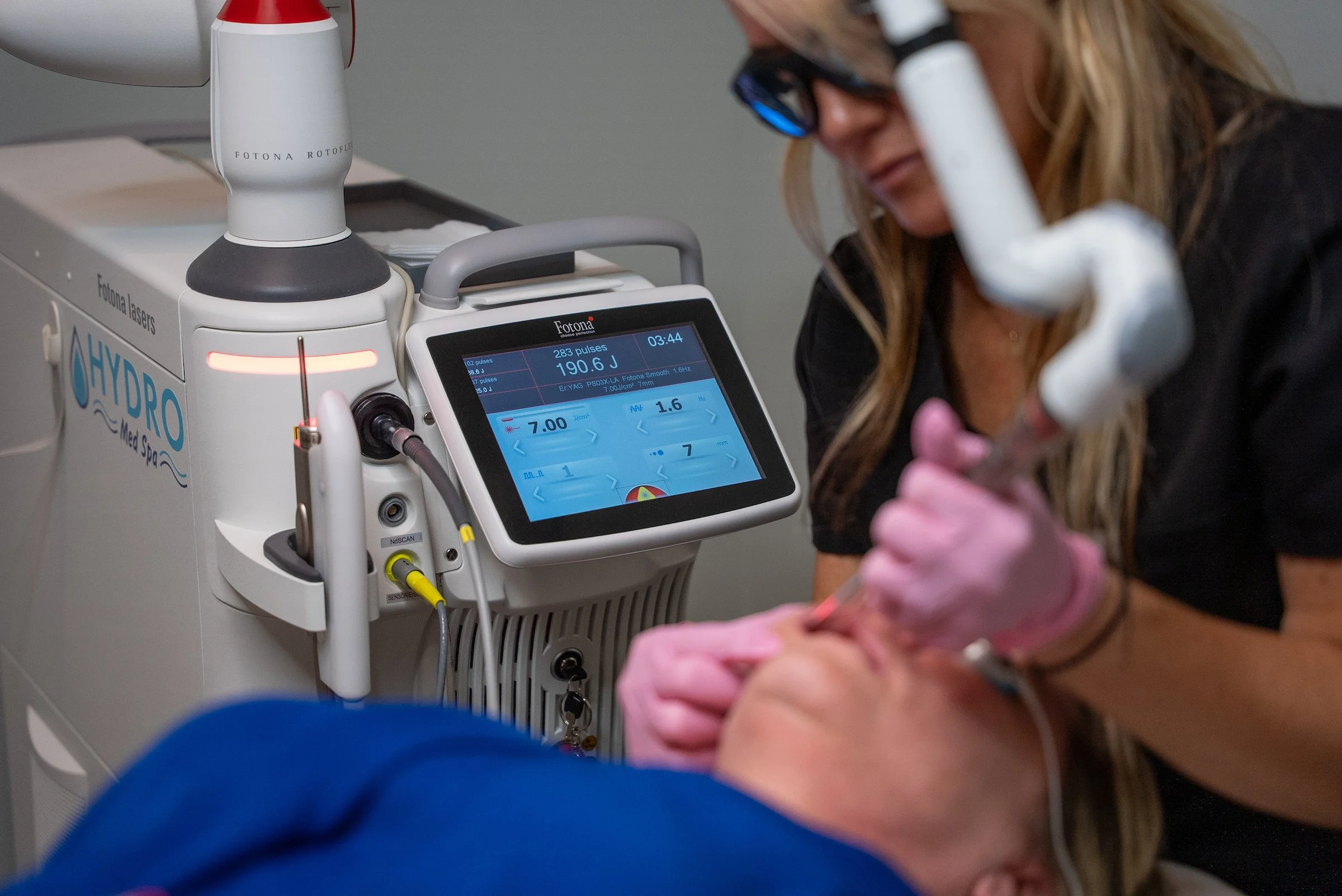 Provider wearing protective eyewear performs a Fotona laser treatment on a patient beside a HYDRO Med Spa laser system