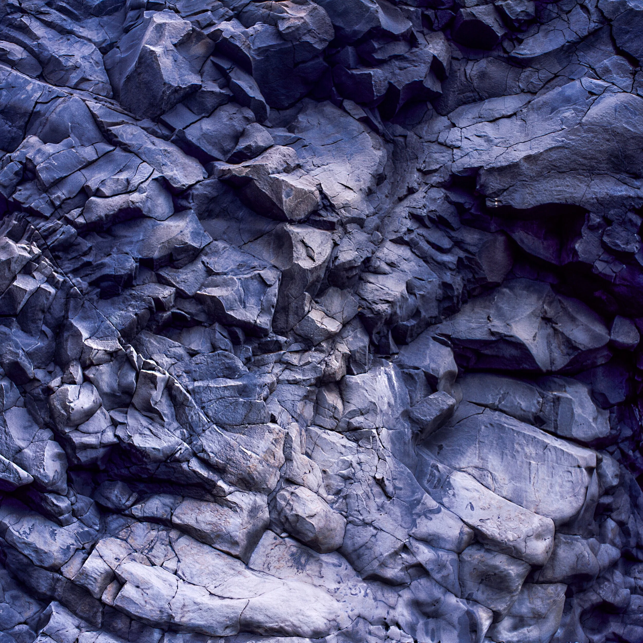 Volcanic Stack, close view of fractured blue grey volcanic rock with angular blocks and deep cracks, layered stone surface shaped by heat and weathering