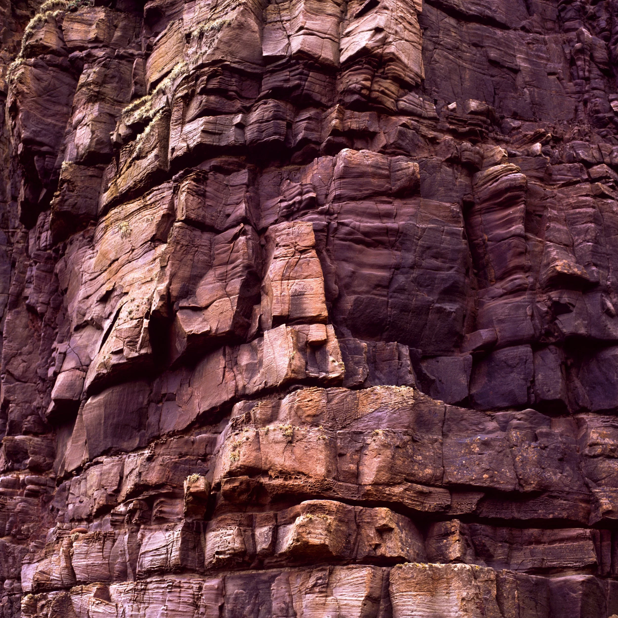 Stacks, close view of deep maroon and pink rock cliff stacked in thick horizontal layers, blocky fractured stone with weathered edges, layered rock texture